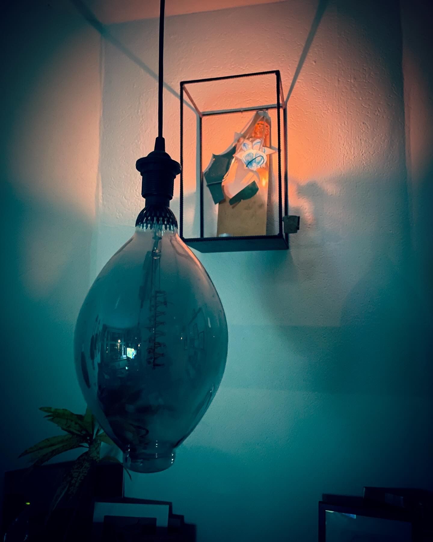 Hanglamp met grote glazen lamp, naast een verlichte vitrine aan de muur.