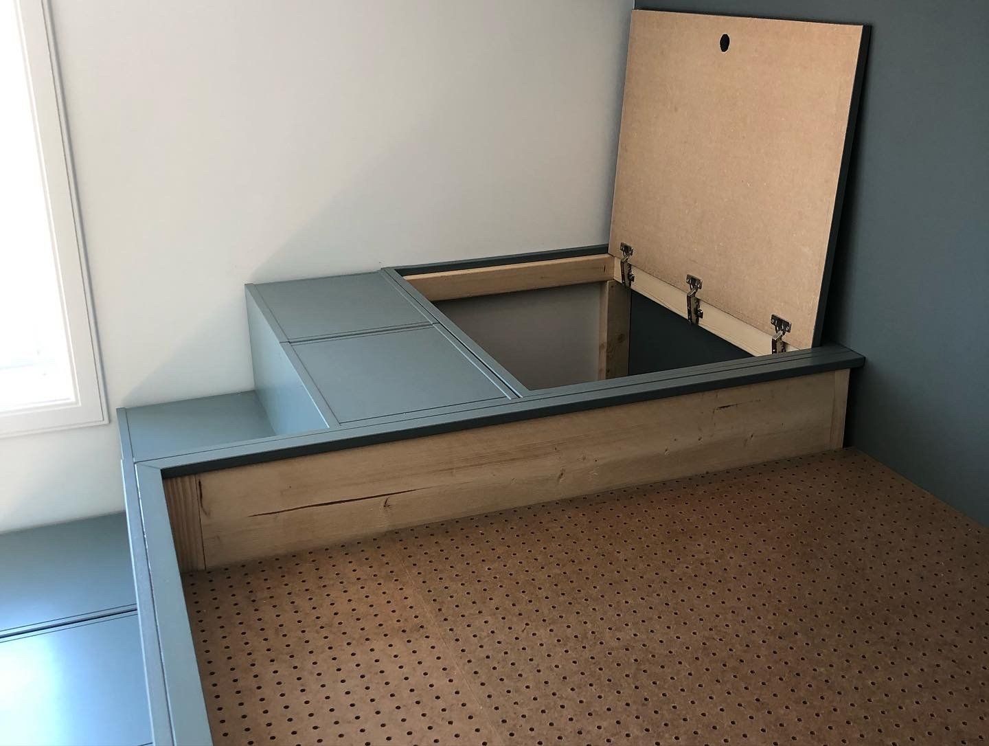 Inbouwbedframe met verhoogd platform en opbergvak met scharnieren. Grijs en natuurlijke houttinten.