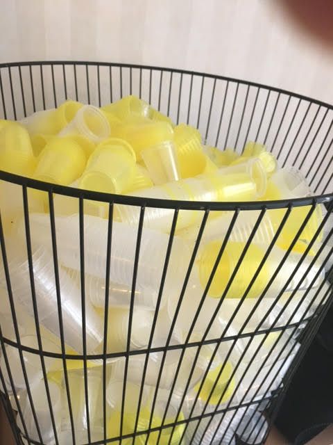Een mand vol gele en witte plastic bekertjes.