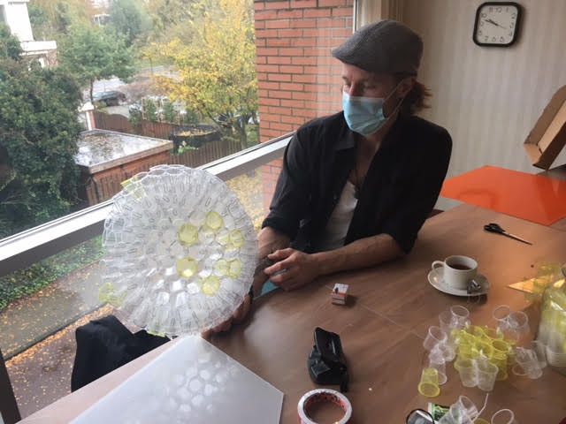 lamp vast die is gemaakt van doorzichtige bekers, terwijl hij aan een tafel bij een raam zit.