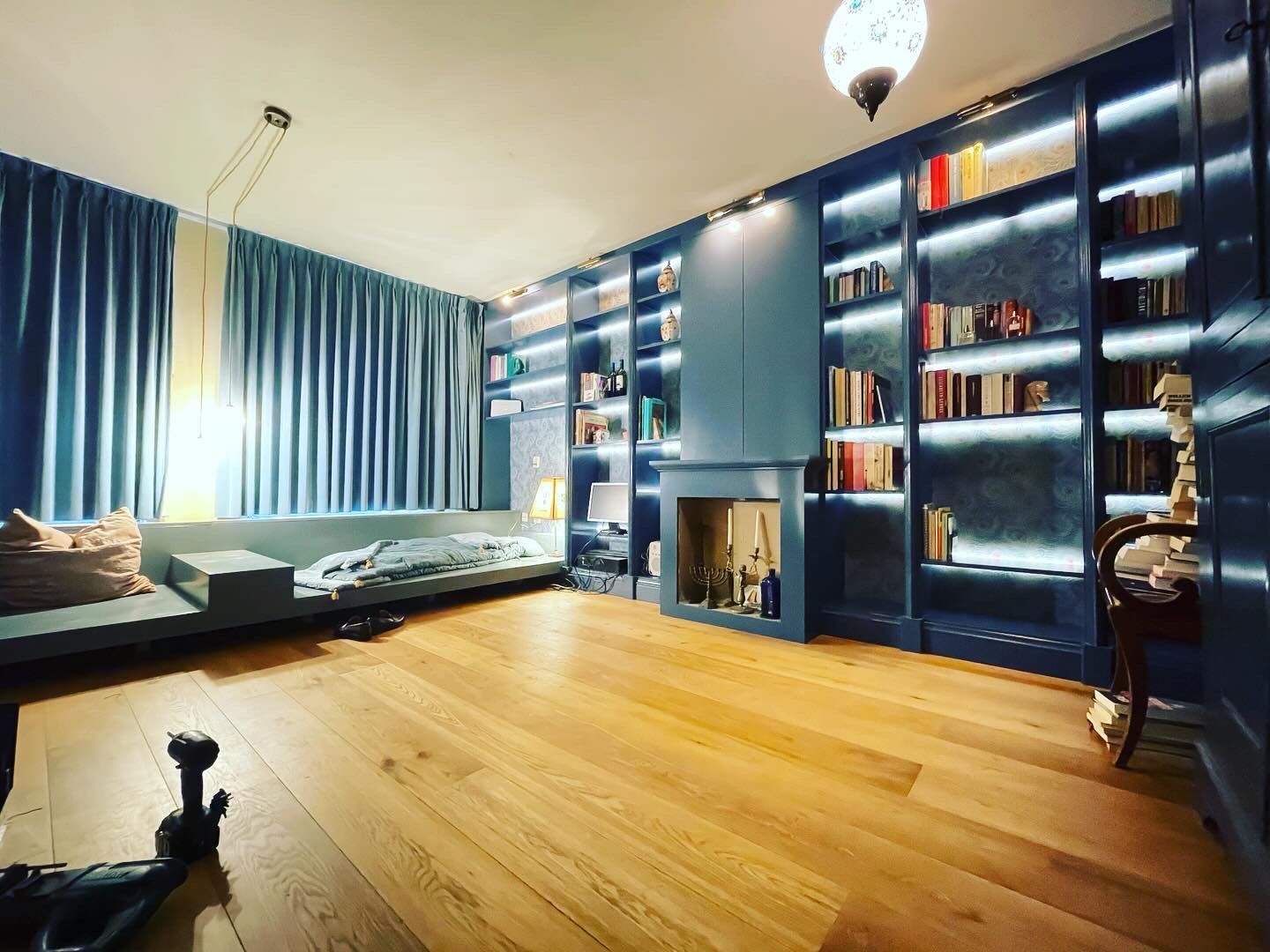 Bibliotheek met blauwe muren, ingebouwde boekenkasten, open haard en houten vloer.