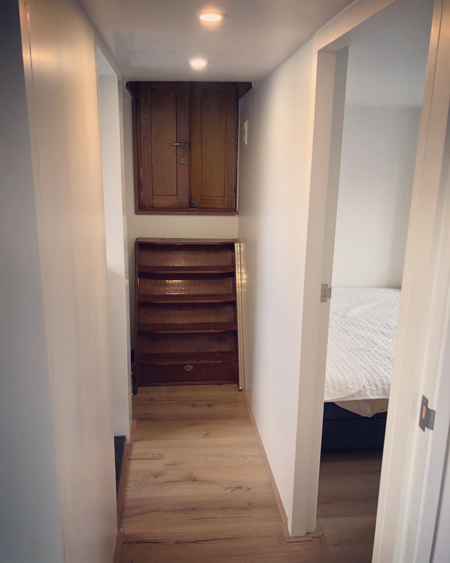Smalle gang met houten traptreden en opbergkast. Deur naar de slaapkamer aan de rechterkant.