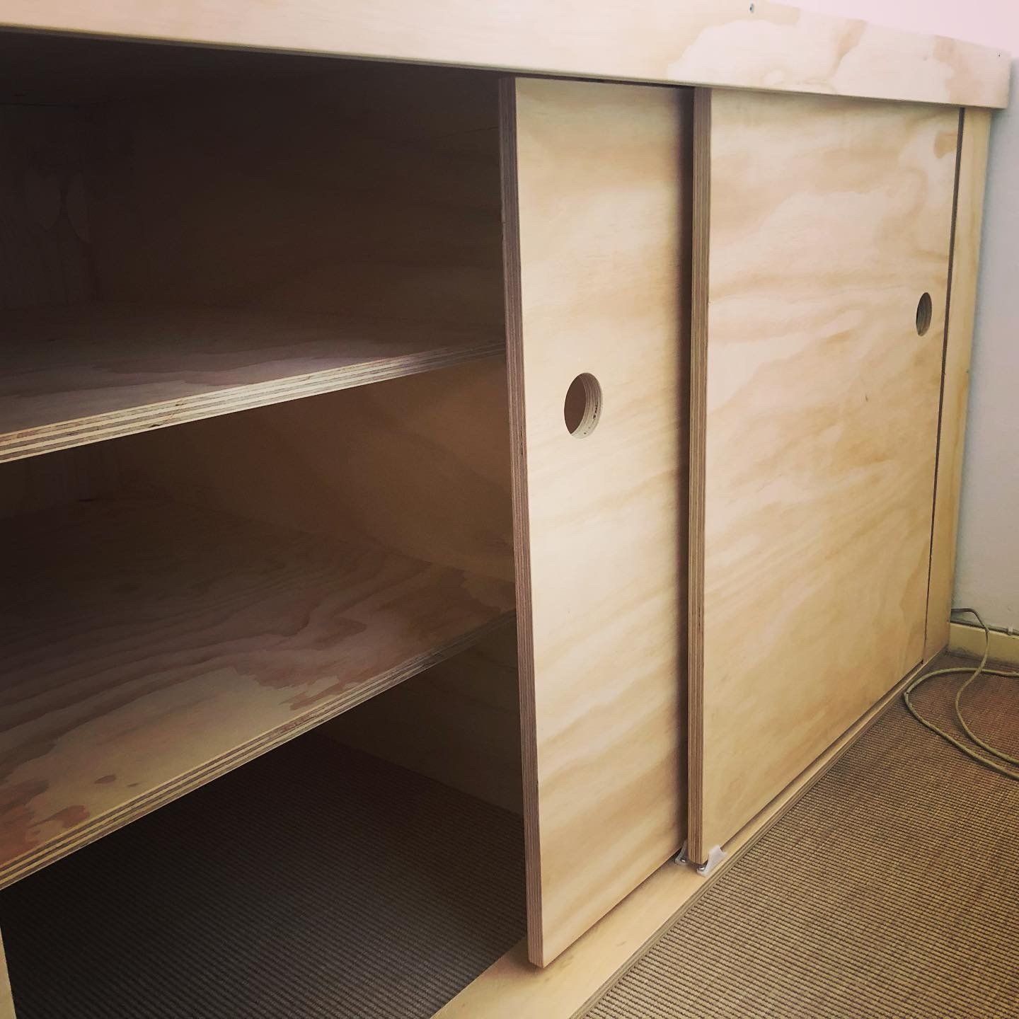 Houten kast met schuifdeuren, planken en ronde handgreepgaten.
