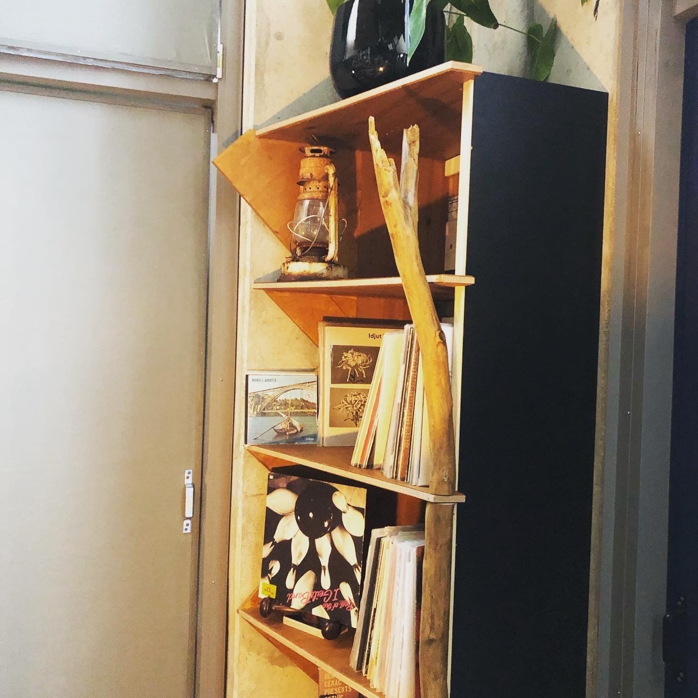 Houten hoekboekenkast met zwarte zijkant, geschikt voor decoratieve voorwerpen en boeken.