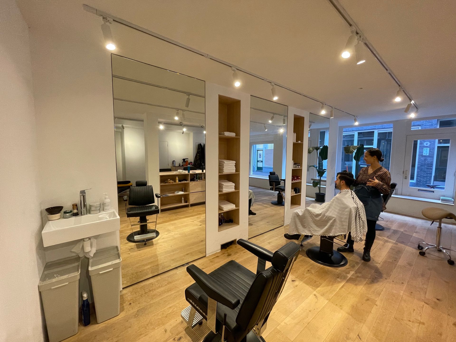 Interieur van een kapsalon met spiegels, kappersstoelen en een klant die geknipt wordt.