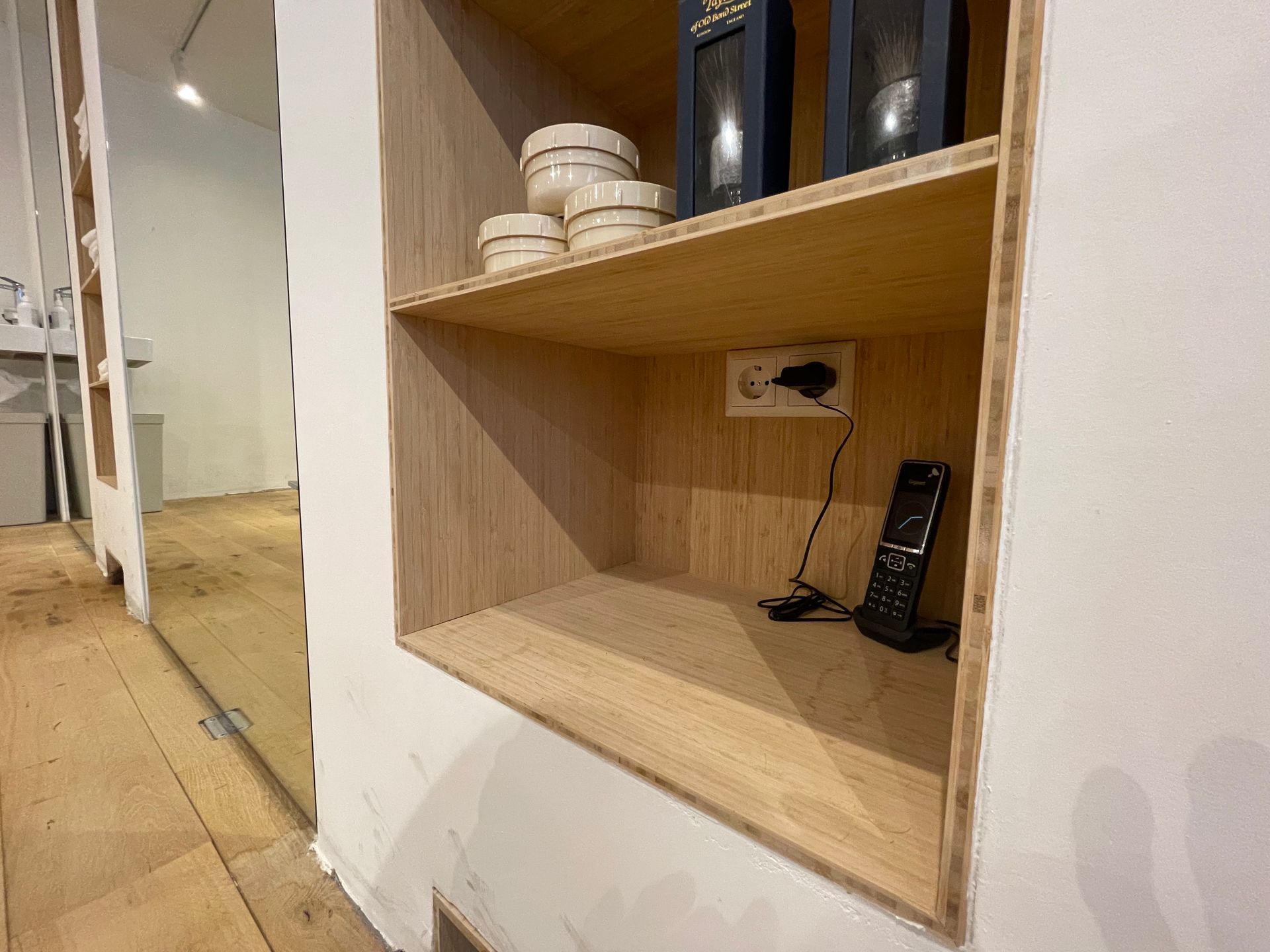Ingebouwde houten plank in een witte muur; biedt ruimte aan luidsprekers, aardewerk en een telefoonoplader.