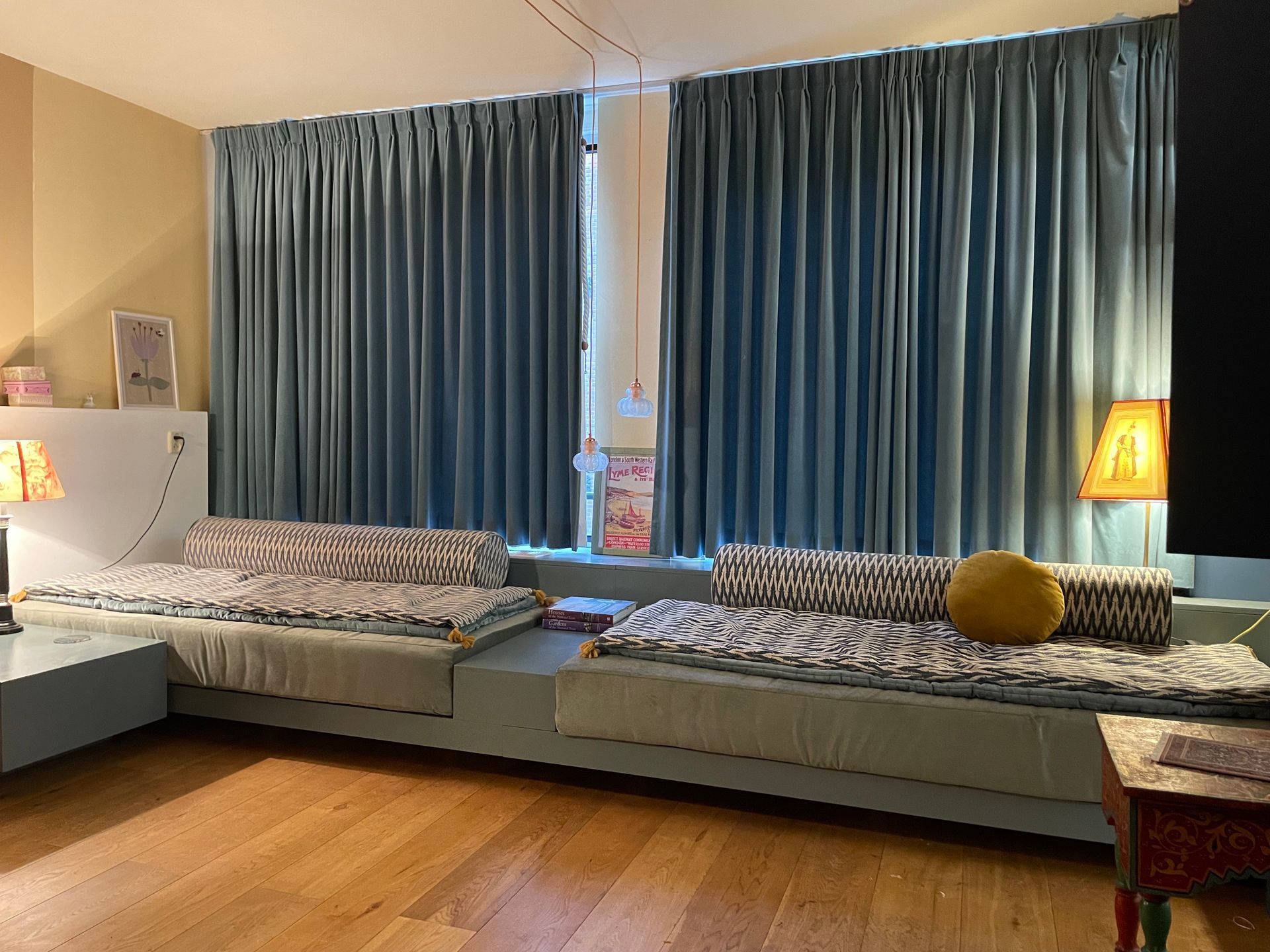 Woonkamer met blauwe gordijnen, lage zitbank, houten vloer en lampen.
