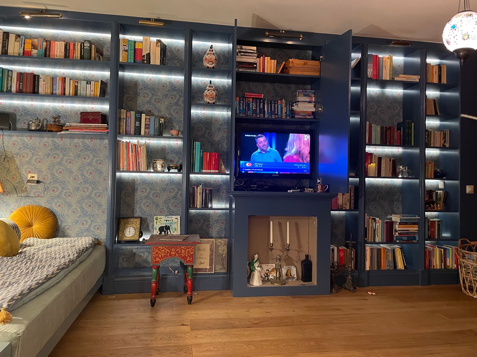 Blauw verlichte boekenkasten met boeken en decoraties omringen een tv in een ingebouwde kast.
