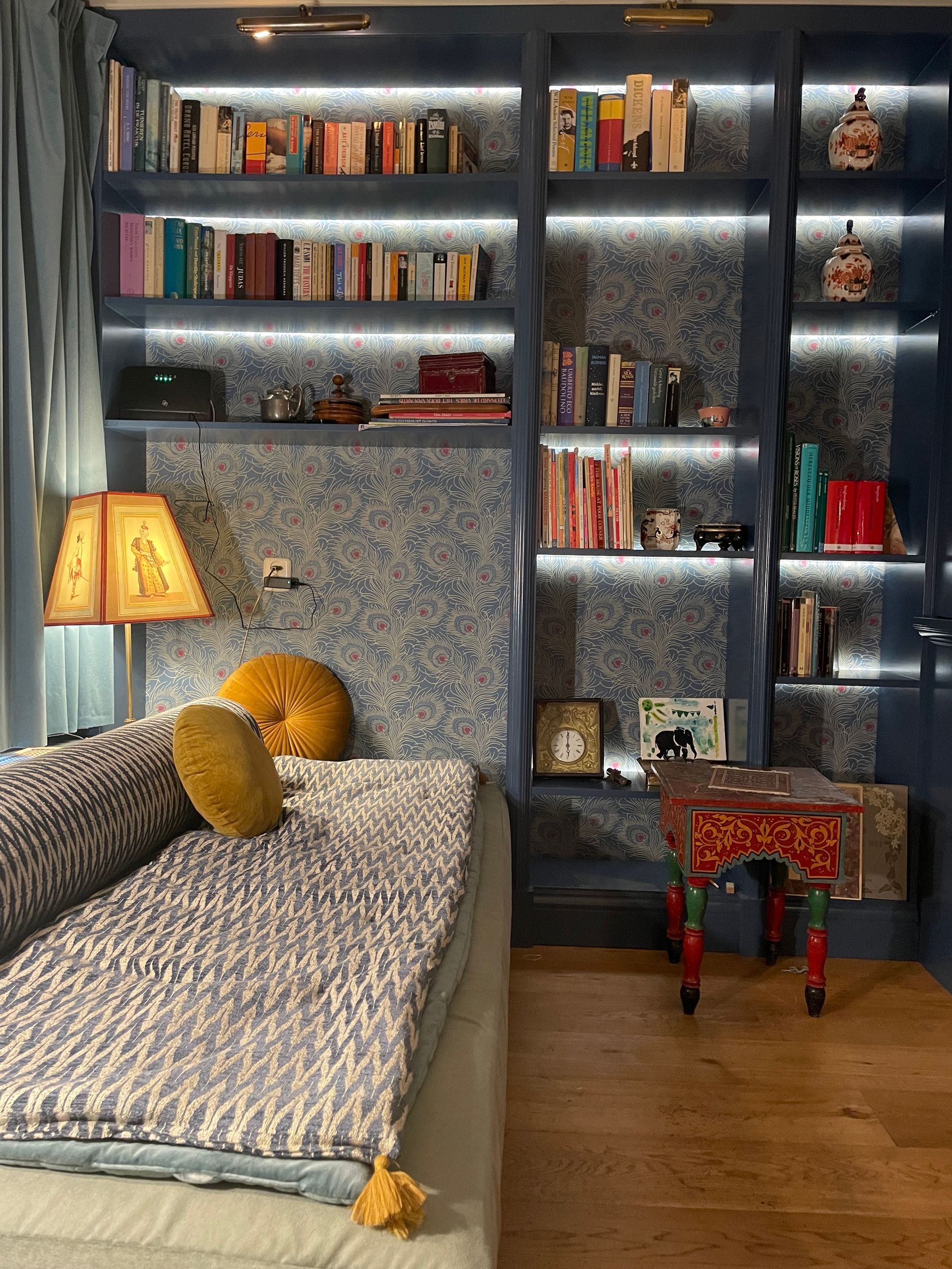 Gezellige slaaphoek met ingebouwde boekenkasten, bed en decoratief bijzettafeltje; in blauwe en gouden tinten.
