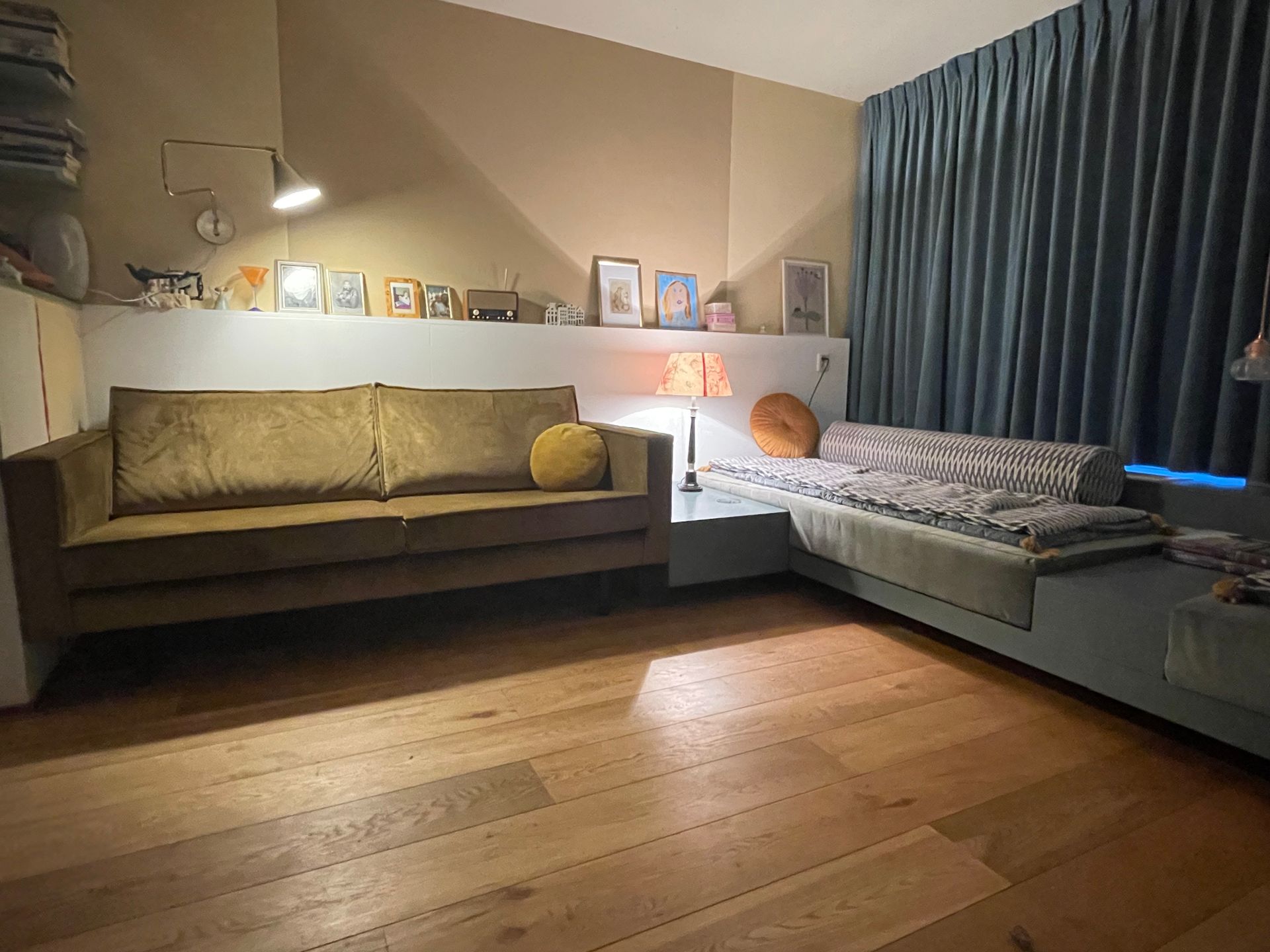Gezellige woonkamer met een bruine bank, een hoekbank en een houten vloer. Gedempte verlichting.