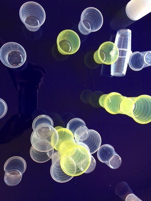 Bovenaanzicht van doorzichtige en gele plastic bekers op een donkerblauwe ondergrond, die langwerpige schaduwen werpen.