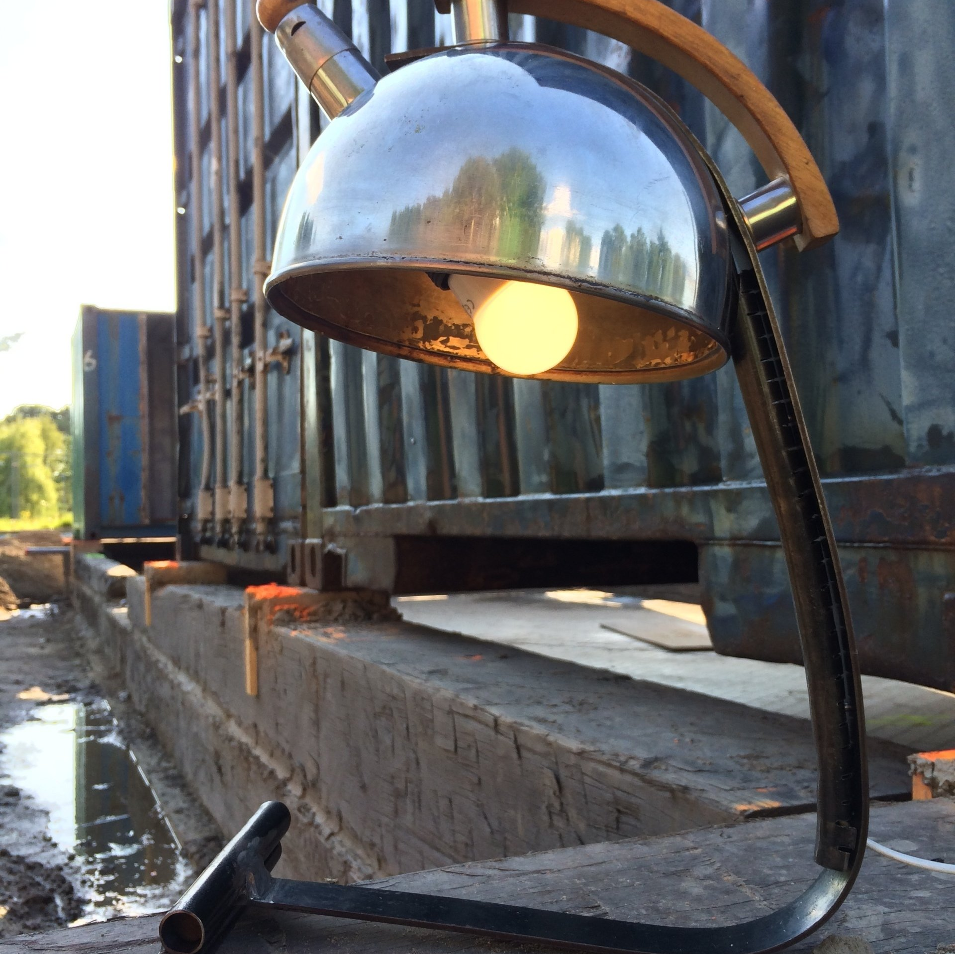 Een lamp gemaakt van een metalen fluitketel, met een houten handvat en een zwarte metalen voet.