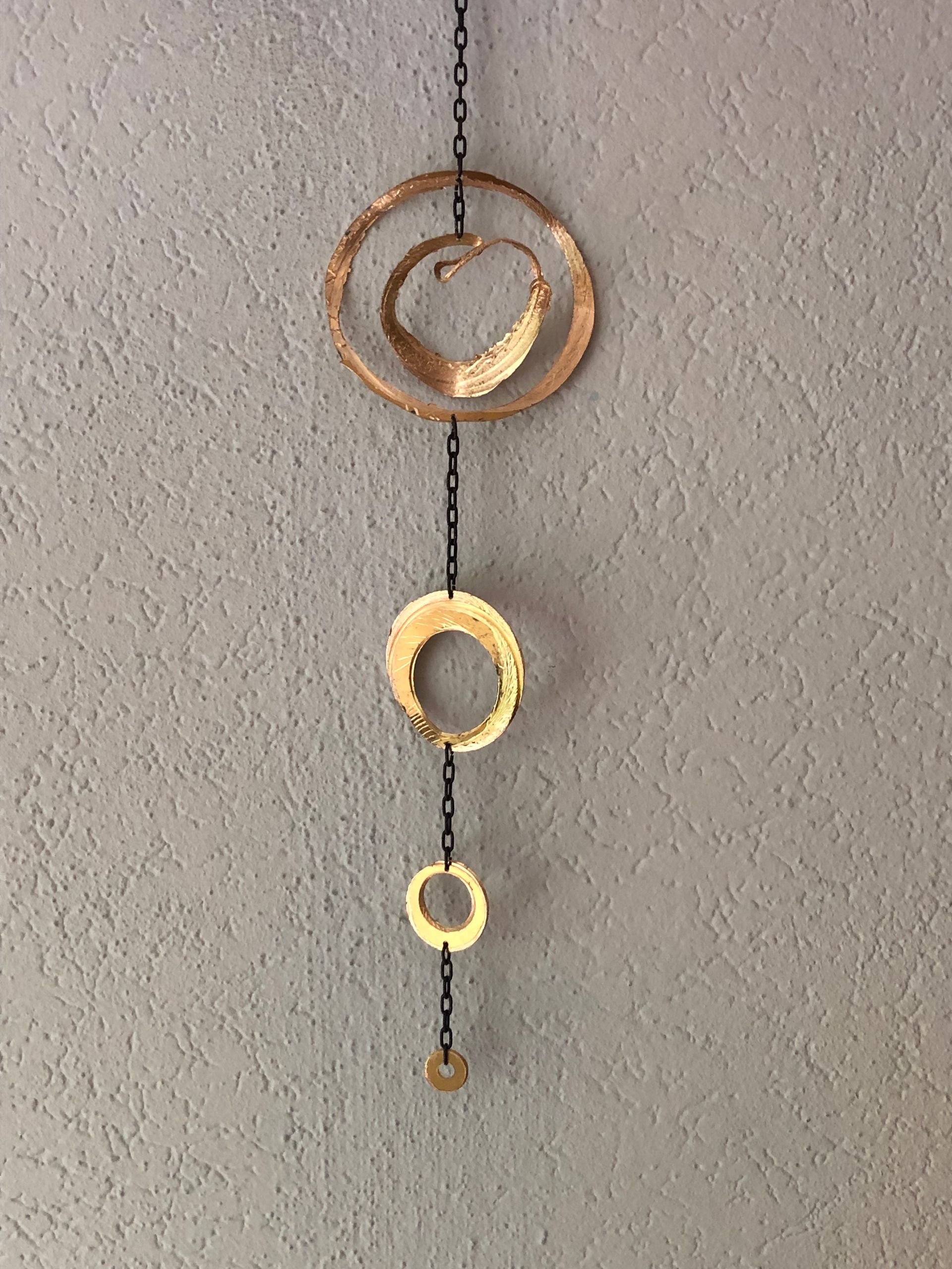 Een goudkleurige metalen sculptuur, hangend aan een grijze muur met structuur, 