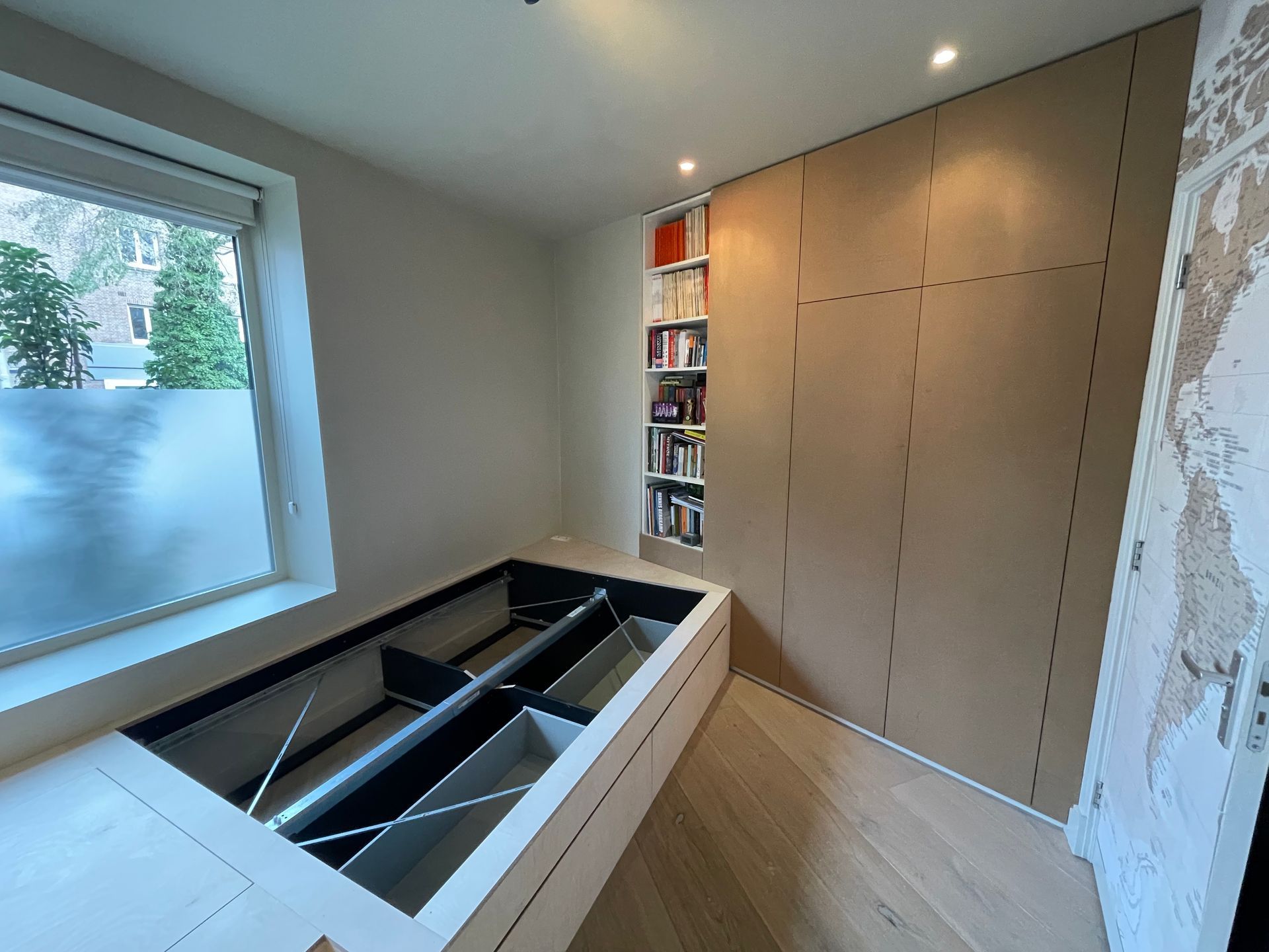 Moderne kamer met ingebouwd bedframe en opbergruimte. Links bevindt zich een raam en rechts ingebouwde boekenkasten.