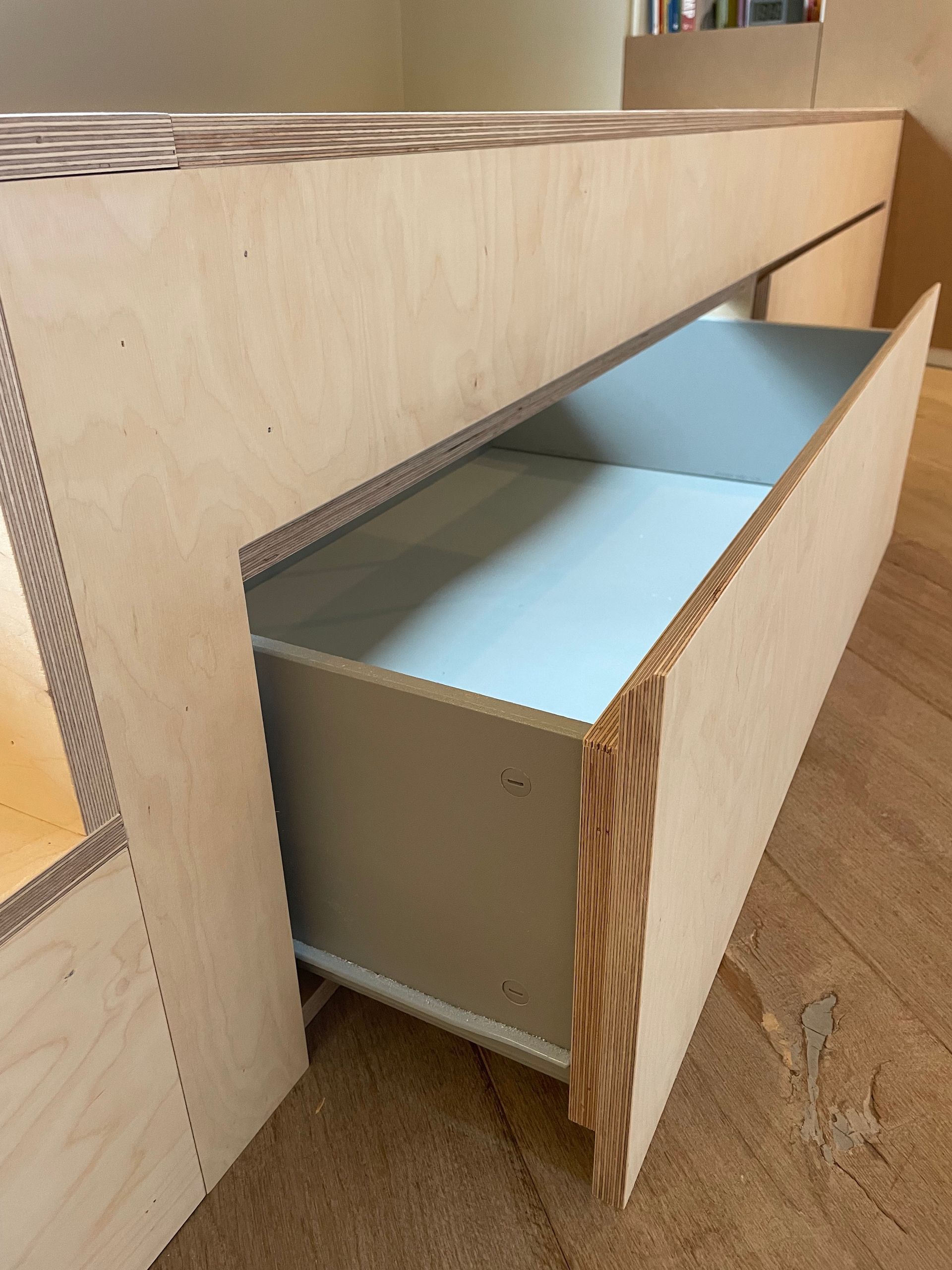 Een gedeeltelijk geopende houten lade in een licht houten kastje. De binnenkant van de lade is lichtgrijs.