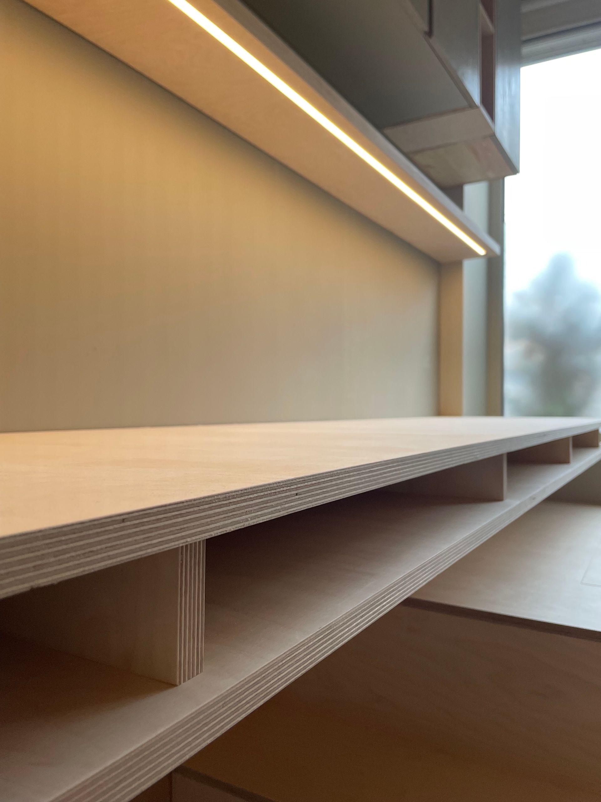 Houten planken met ingebouwde verlichting, tegen een lichtgekleurde muur, vlakbij een raam.