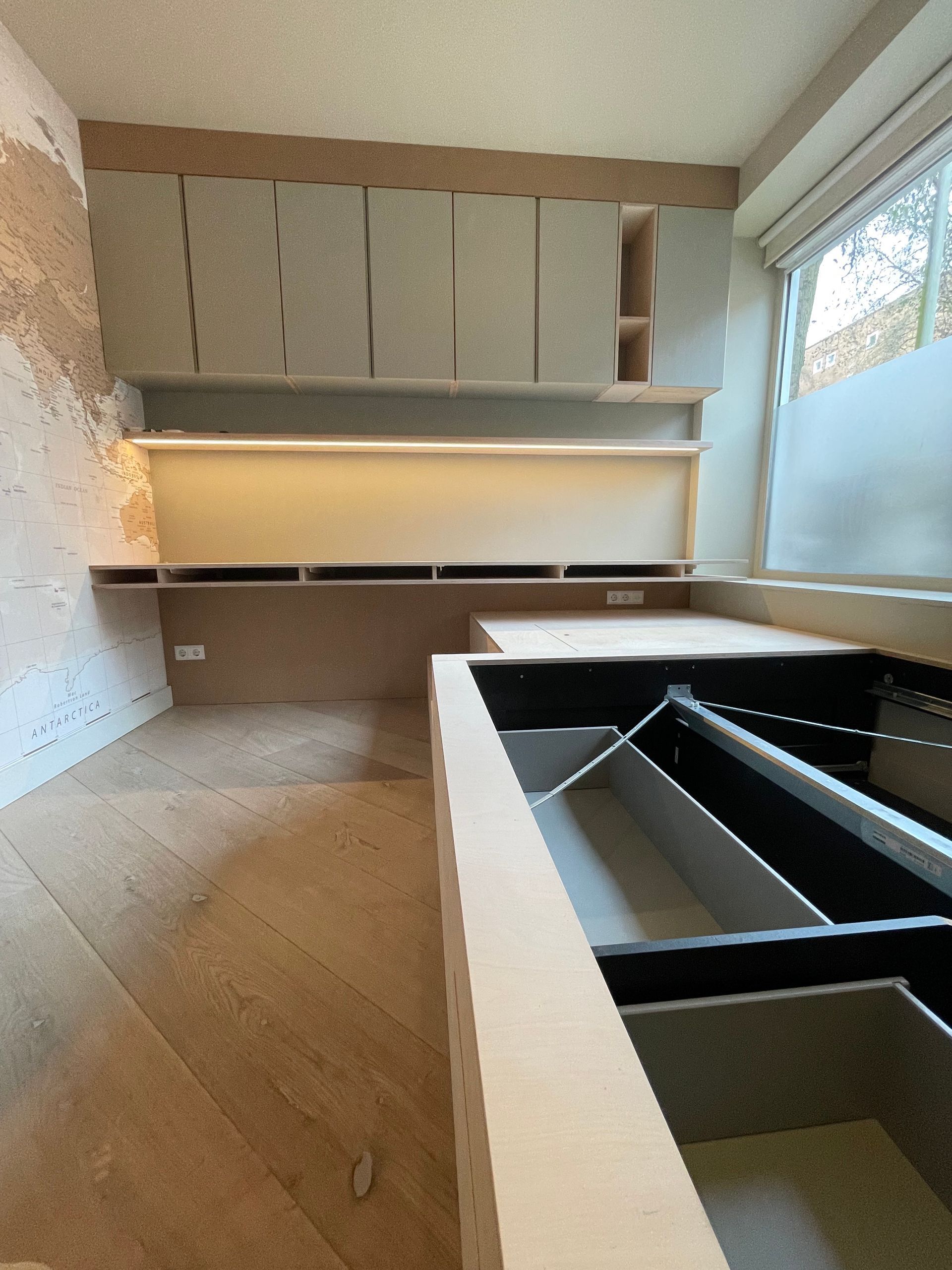 Ingebouwde kasten en planken in een ruimte in aanbouw, met houten frame en lichtgrijze deuren.
