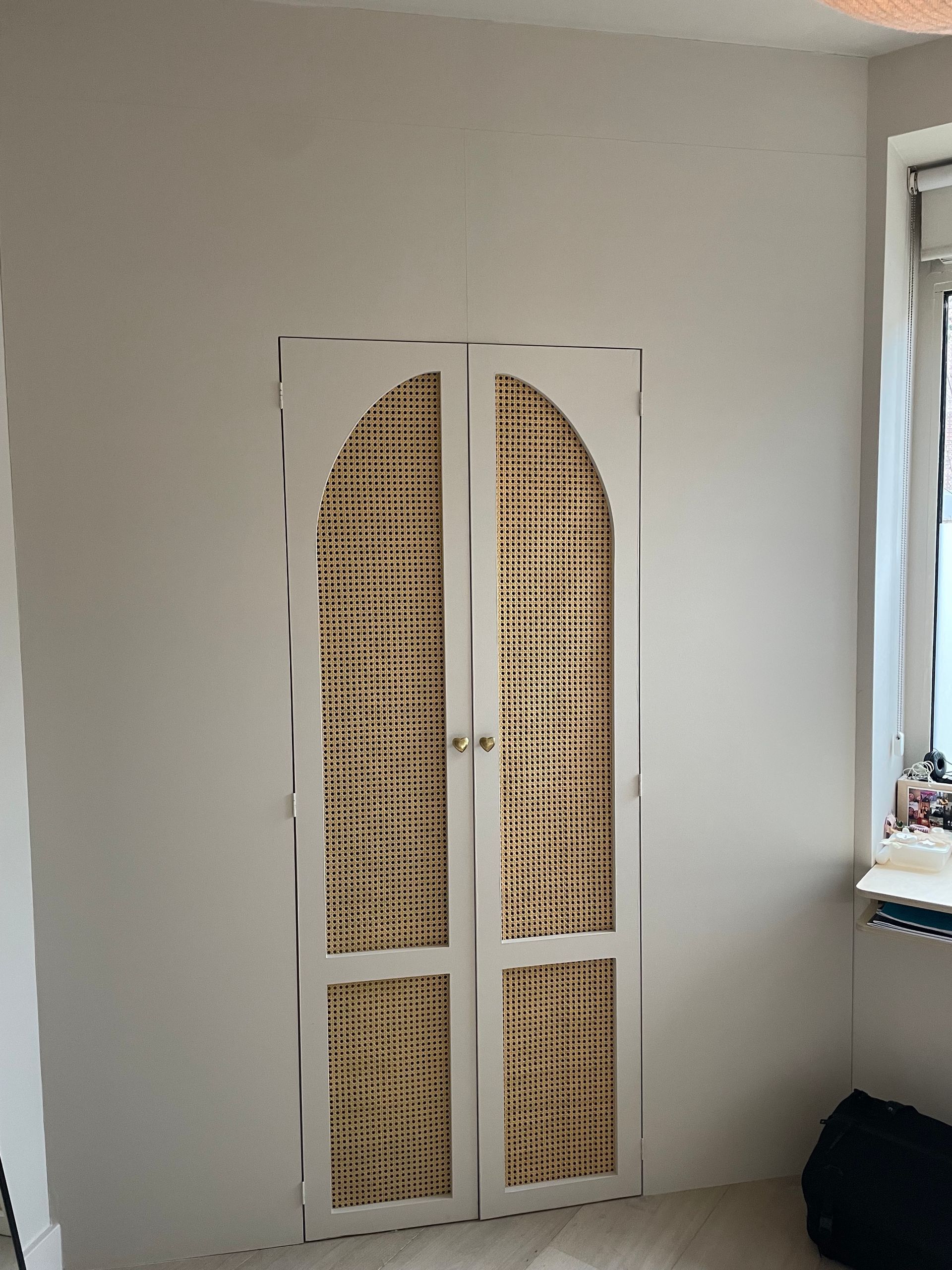 Witte, gebogen kastdeuren met ingelegde rieten panelen tegen een witte muur.