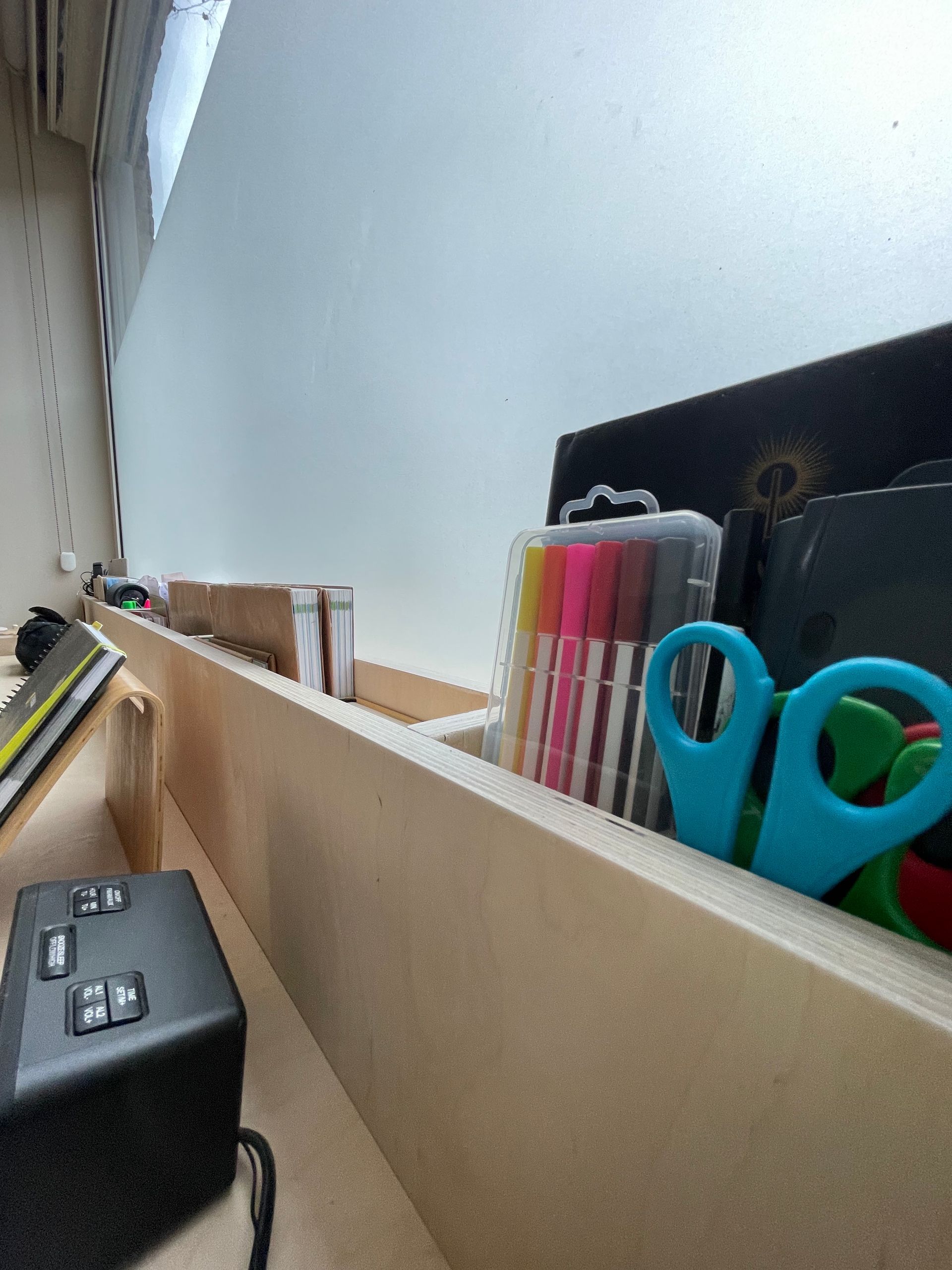 Plank met kantoorartikelen: stiften, scharen, notitieboekjes en een zwarte doos.