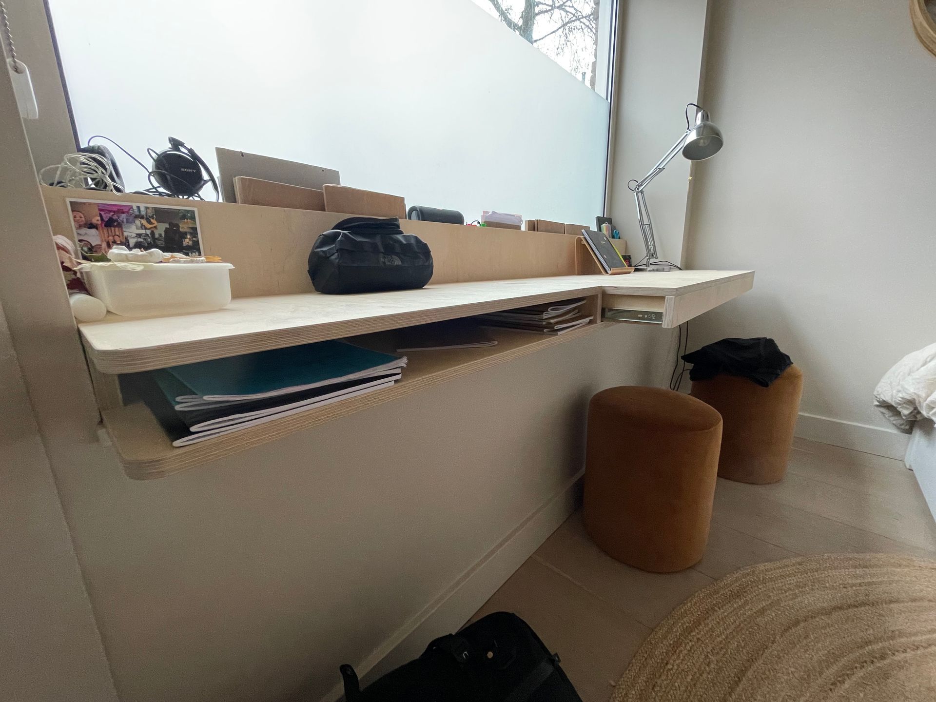 Ingebouwd houten bureau met een plank en een raam met uitzicht op matglas, met krukjes en een vloerkleed.