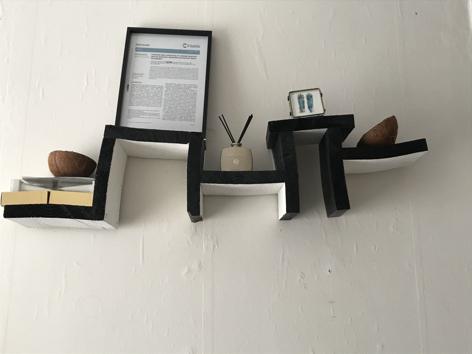 Een plank met zwart-wit design aan een witte muur, waarop decoraties en ingelijste documenten staan.