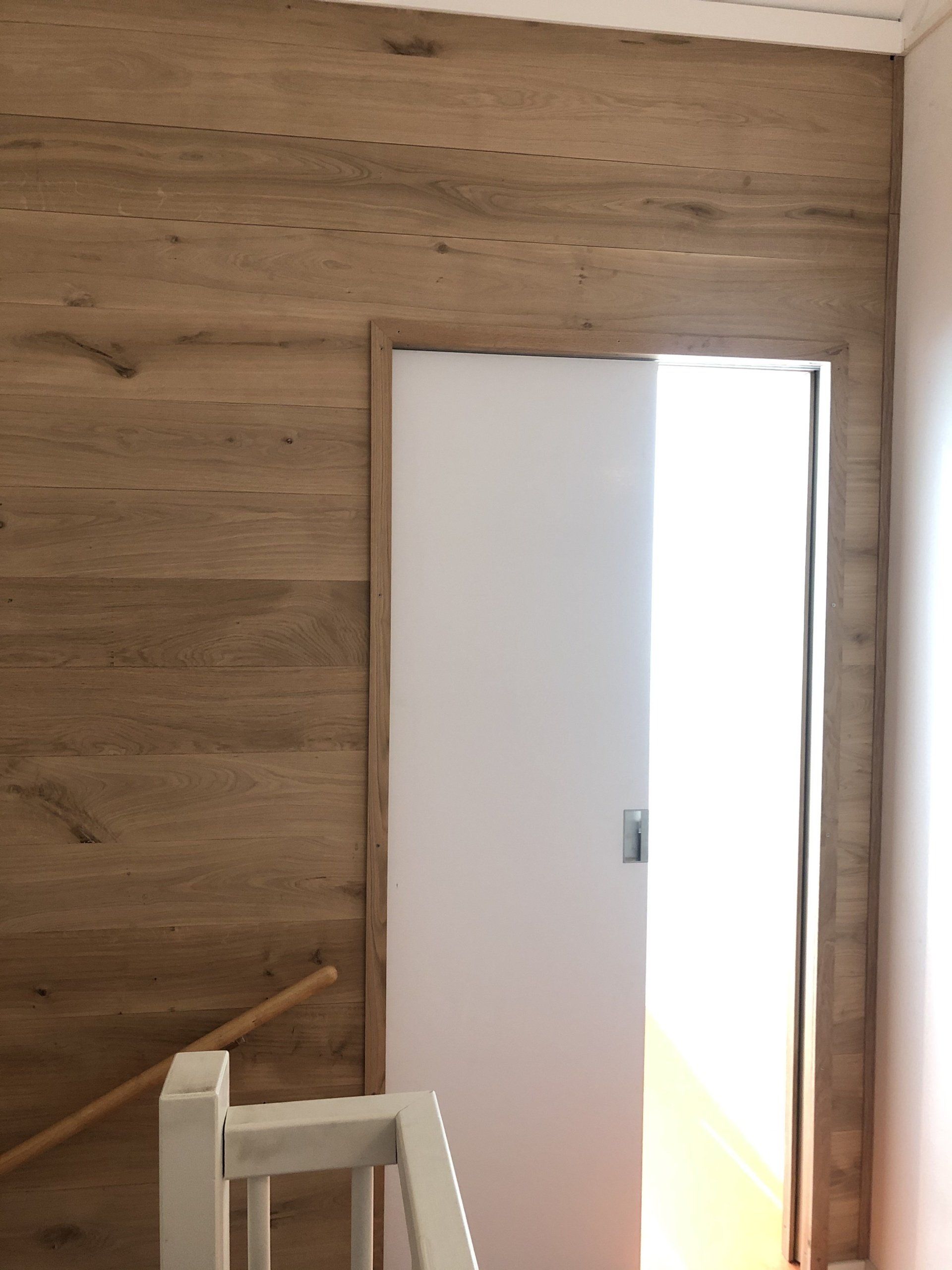 Witte schuifdeur open, ingebouwd in een houten lambrisering. Trapleuning zichtbaar.