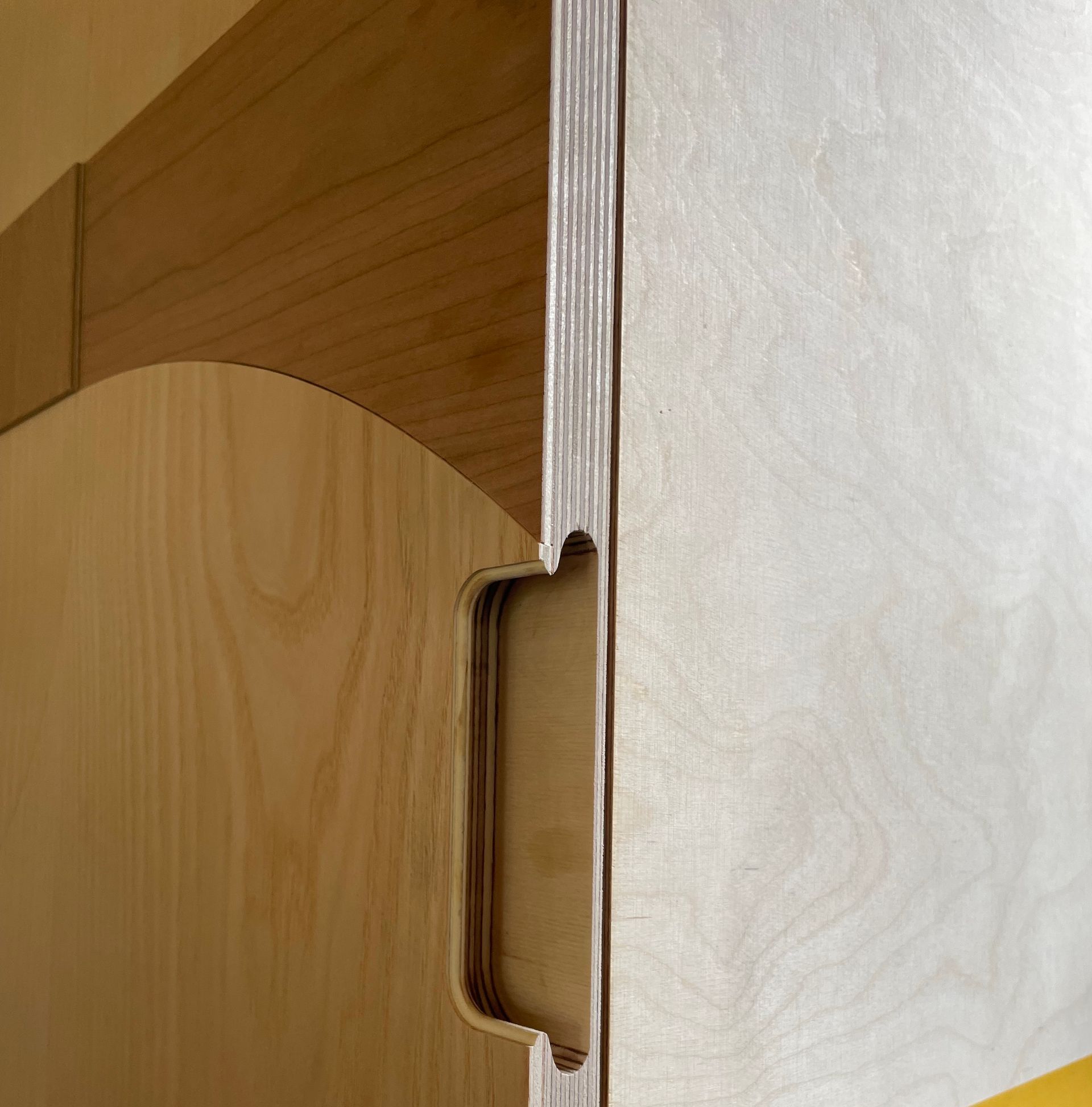 Detailopname van een houten kastdeur met een verzonken handgreep. Lichte houttinten overheersen.
