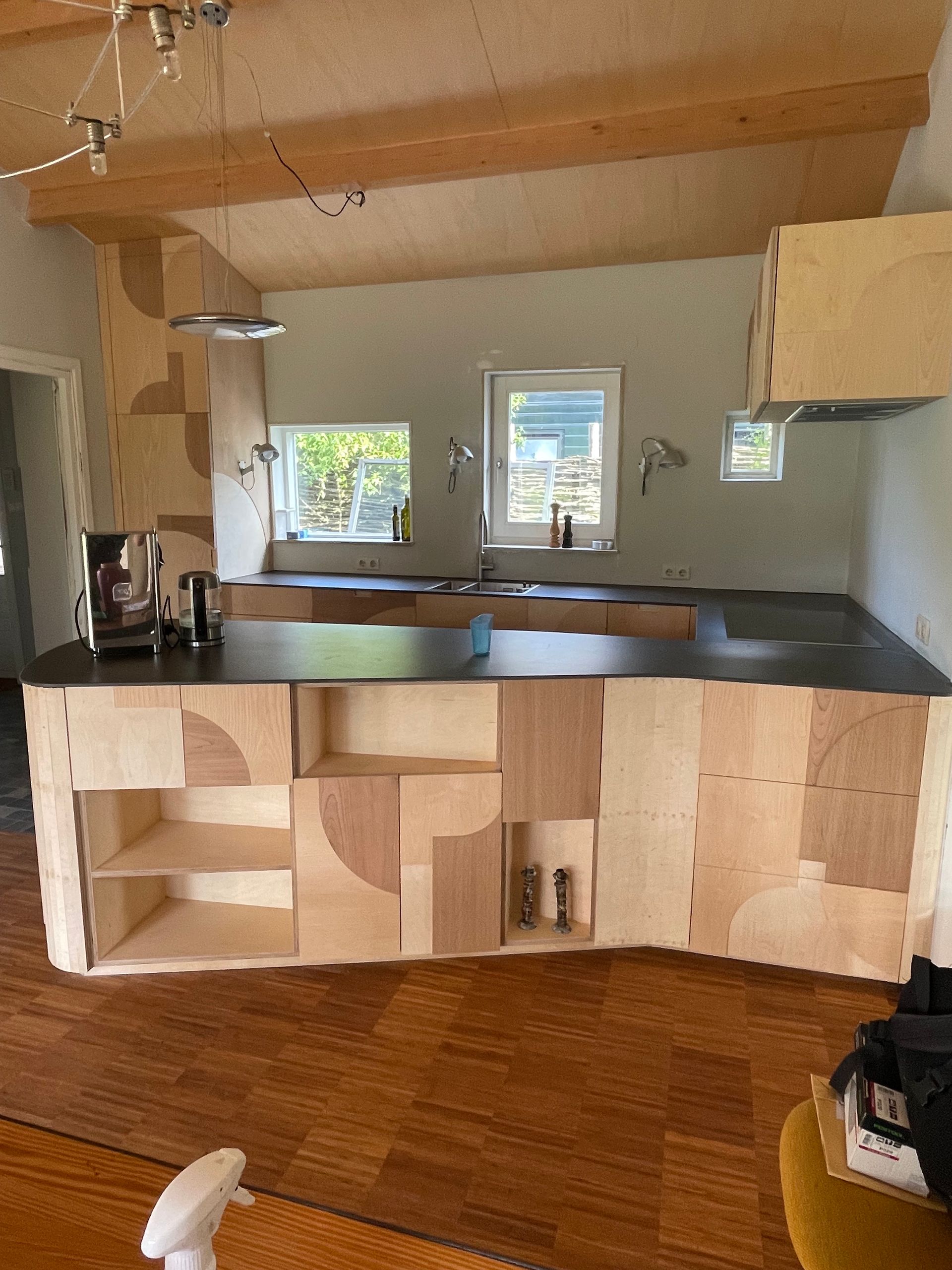 Keuken met lichte houten kasten, donkere werkbladen en houten vloer; een uniek geometrisch ontwerp.
