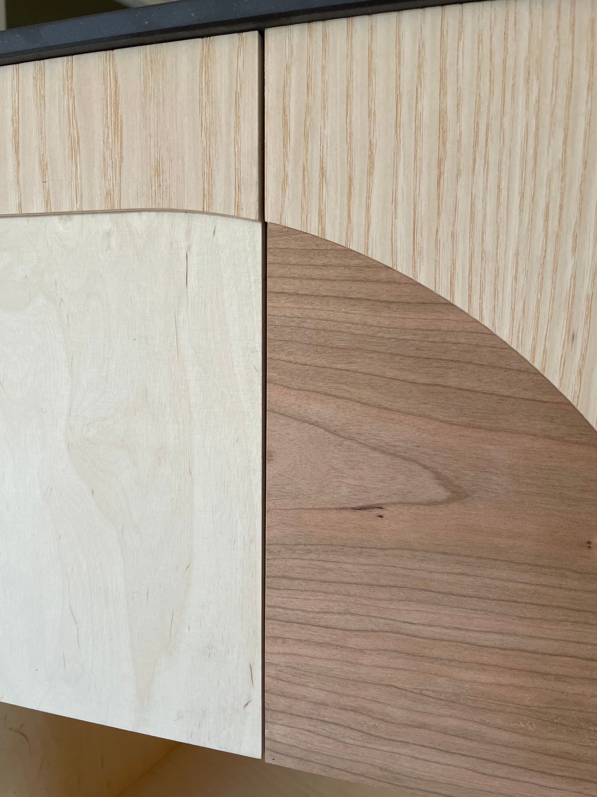 Detailopname van houten kastdetails. Lichte en donkere houten panelen met een gebogen gedeelte. Zwarte afwerking.