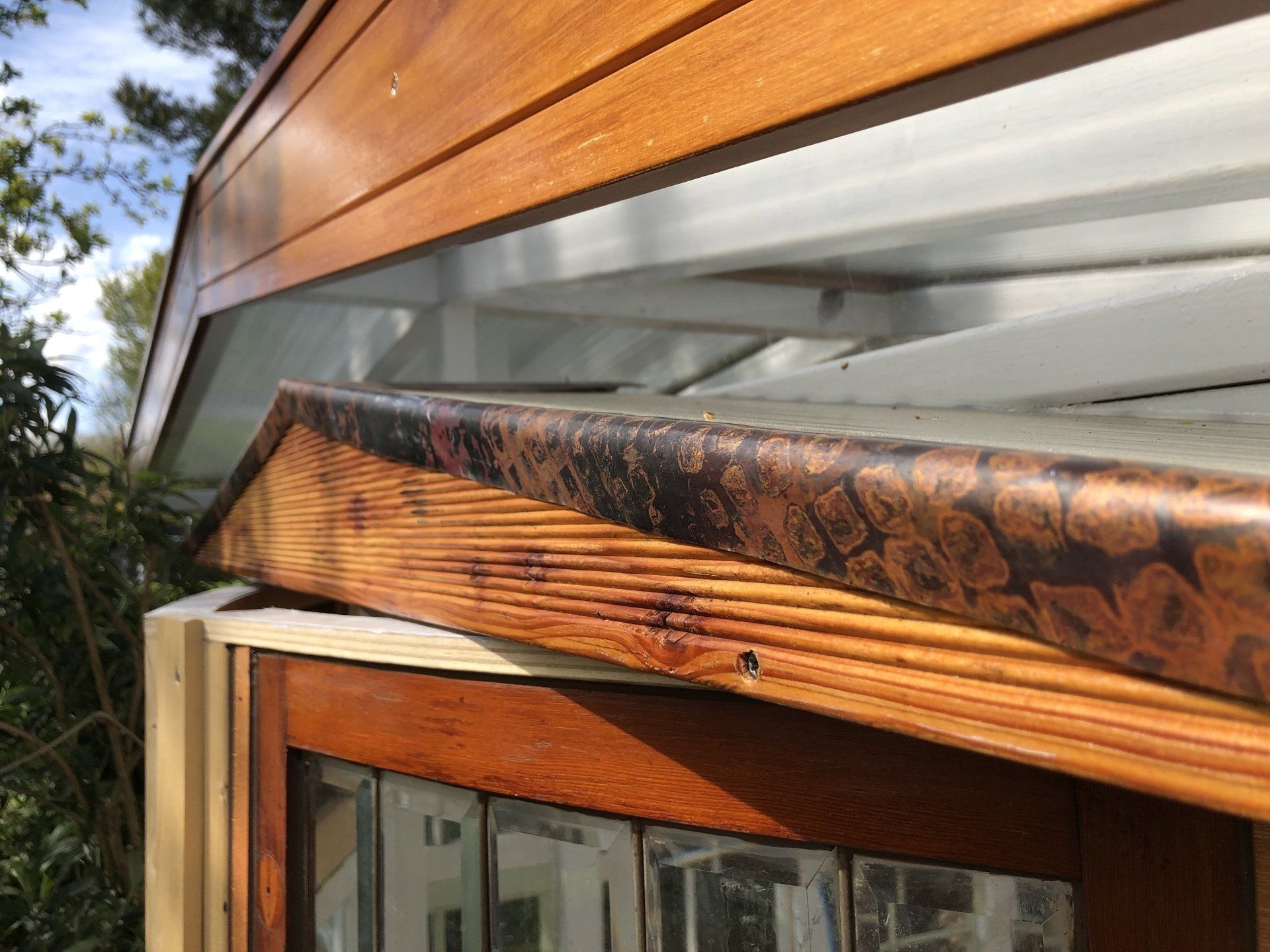 Detailopname van het dak van een houten gebouw met koperen details en een raamkozijn.
