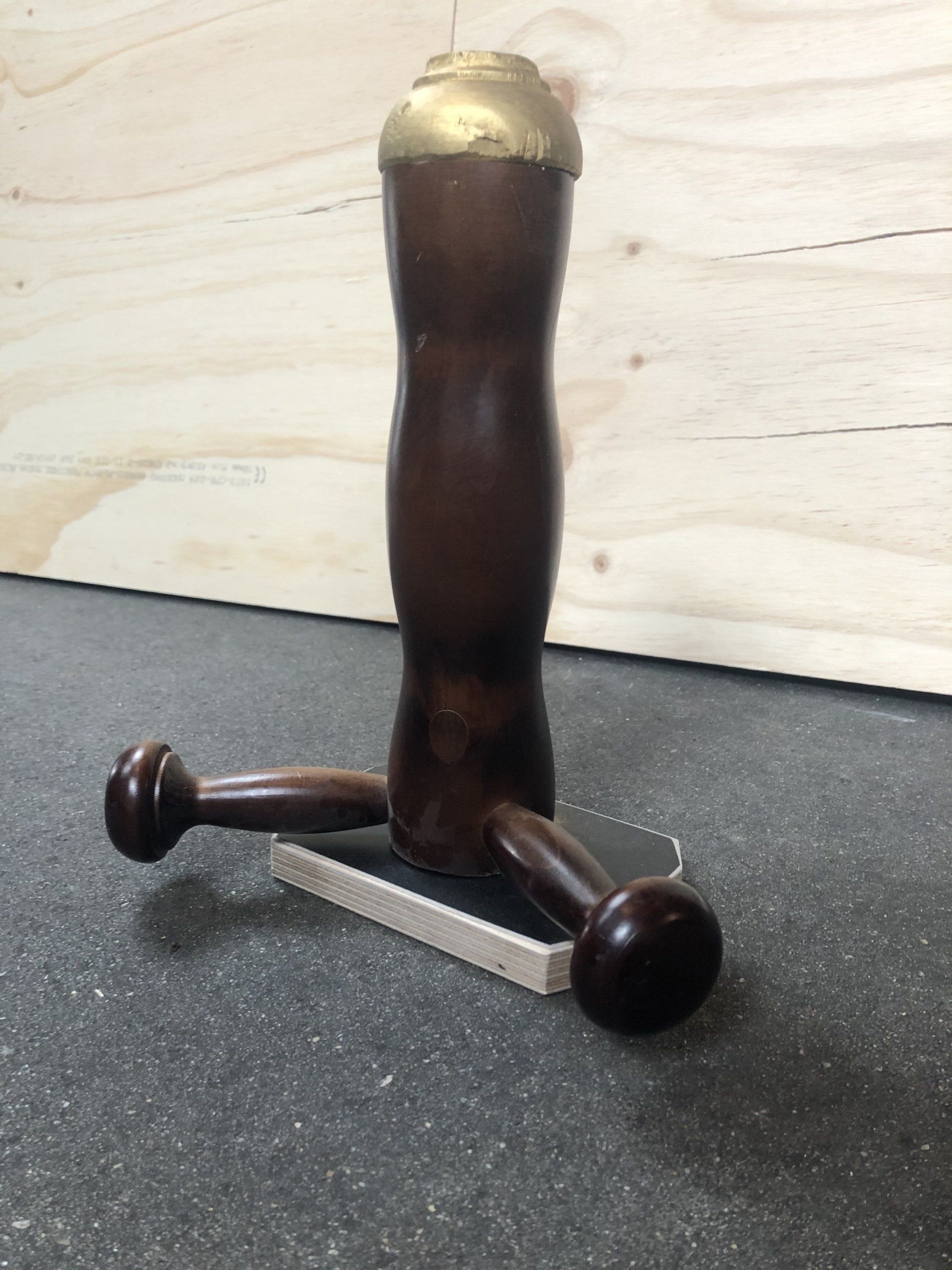 Houten hamer met een messing kop en twee zijknoppen, rustend op een klein, rechthoekig platform.