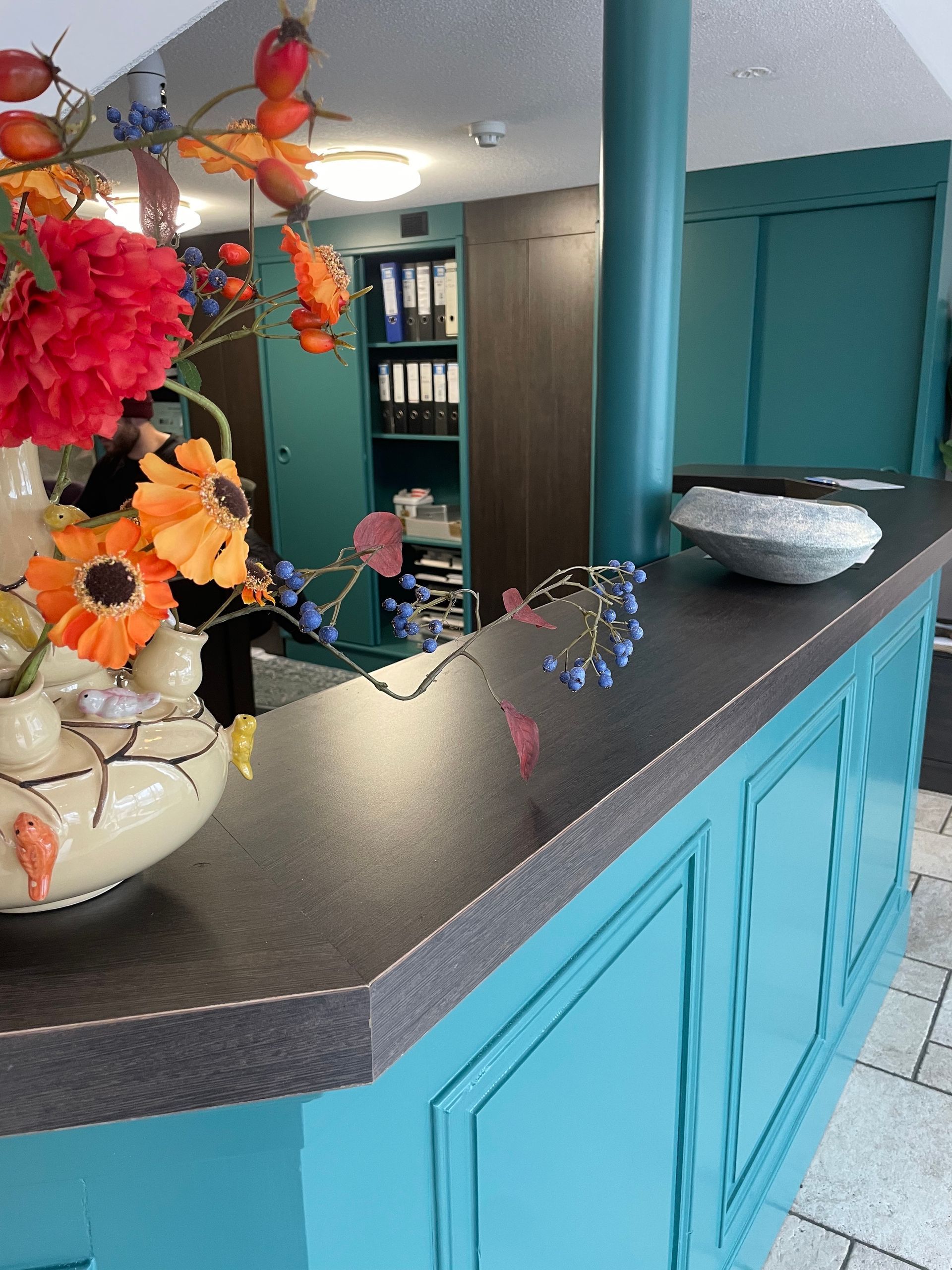 Receptiebalie met turquoise accenten, een donker aanrechtblad en een bloemstuk.