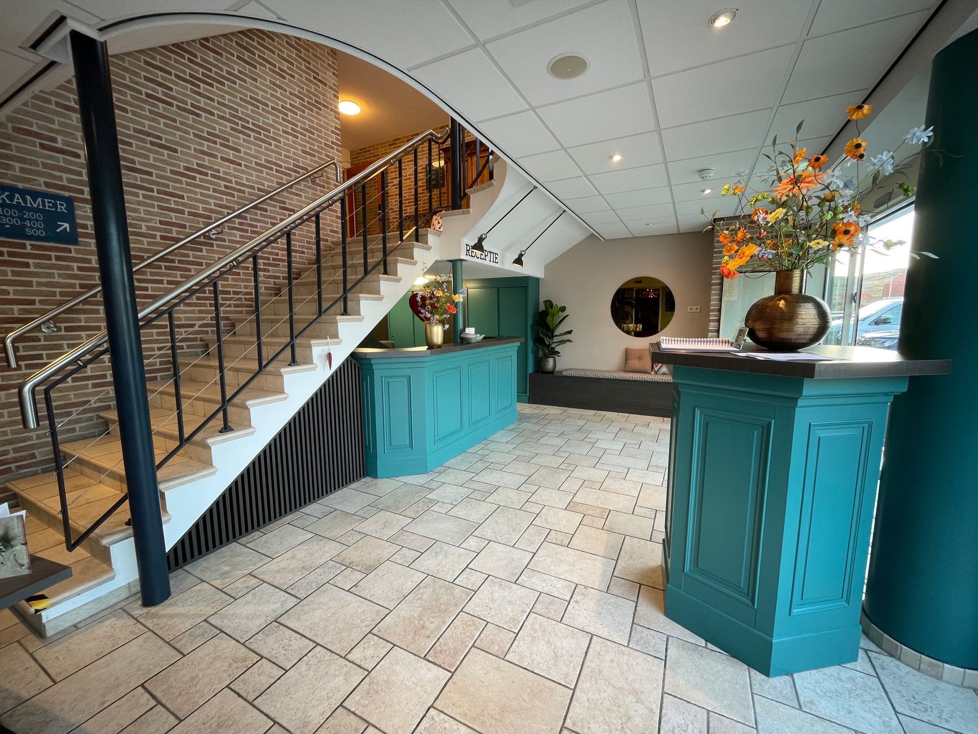 Ontvangstgedeelte met turquoise accenten, trap en bloemstuk.