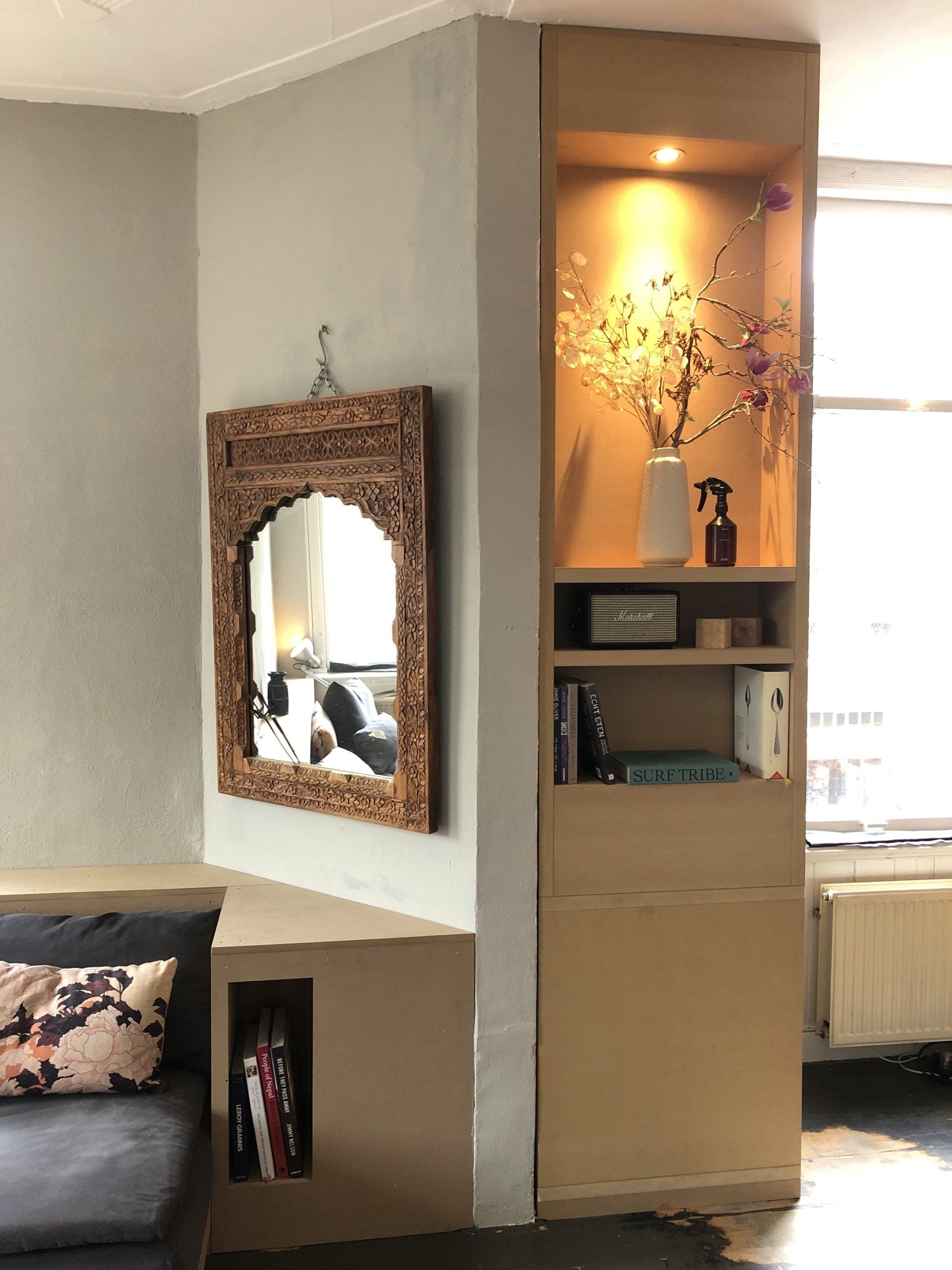 Woonkamerhoek met ingebouwde planken, spiegel en bank; aangevuld met decoratieve objecten en planten.