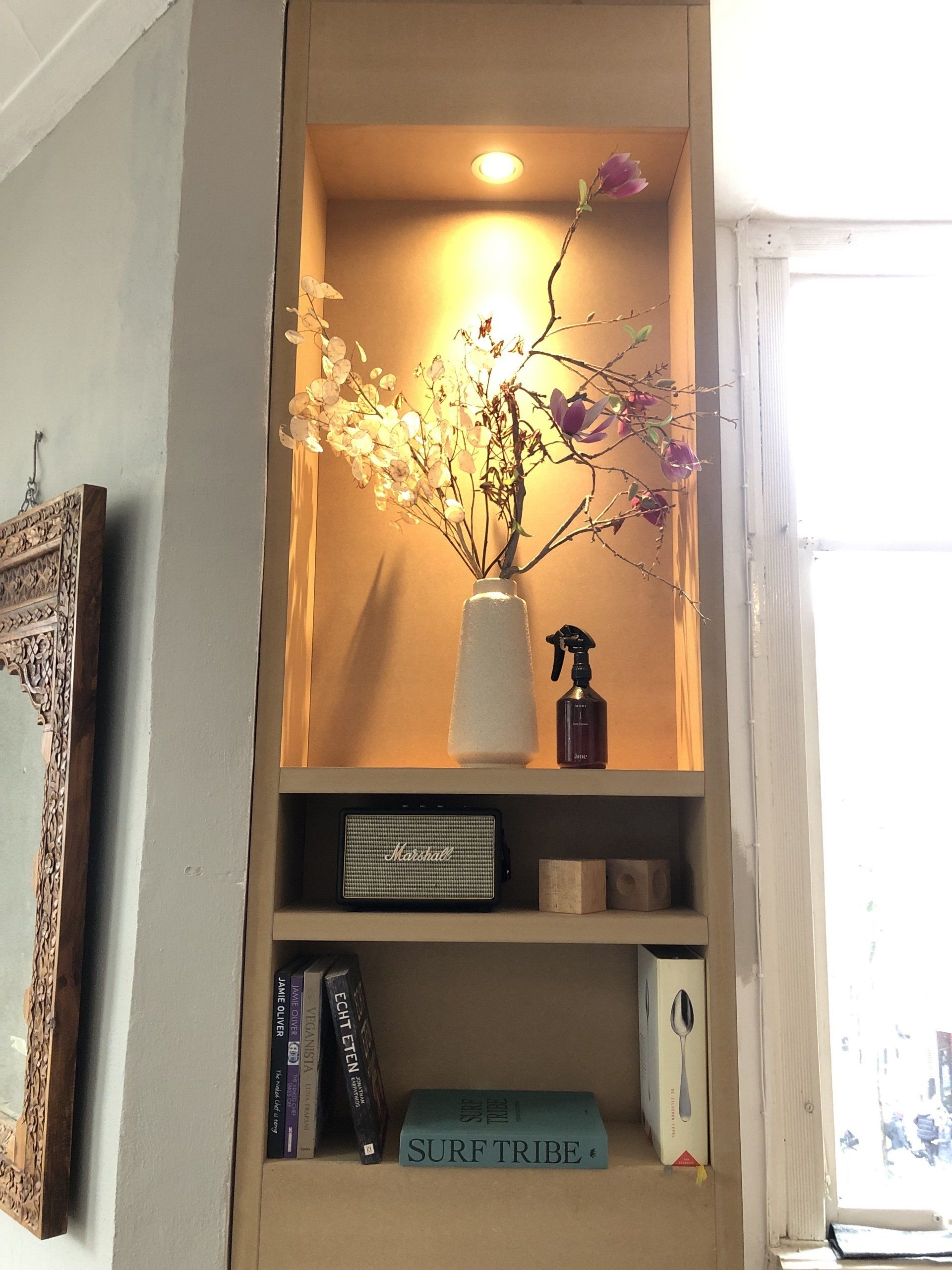 Ingebouwde houten plank met bloemen in een vaas, boeken en decoratie, verlicht door warm licht.