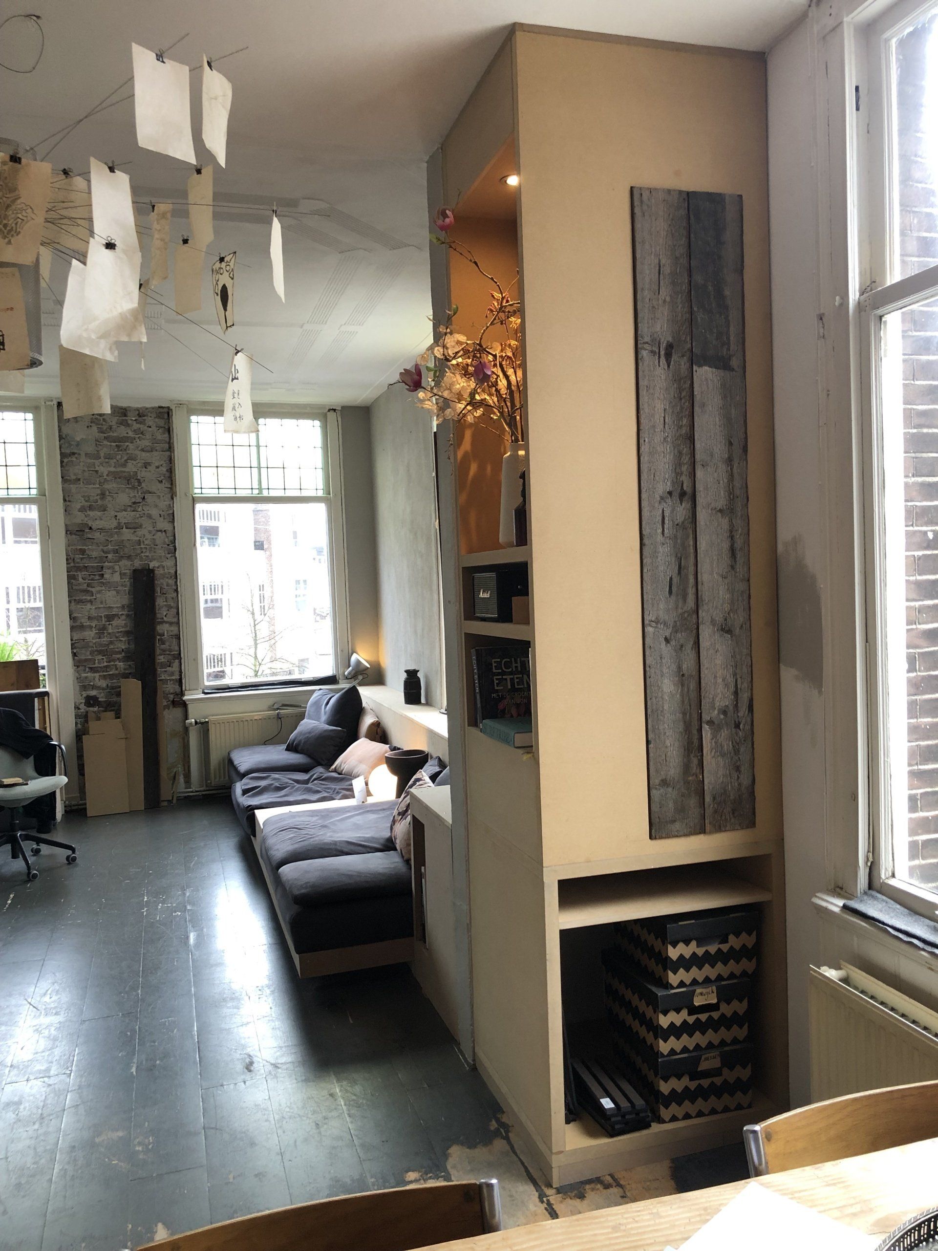 Woonkamer met een ingebouwde boekenkast, een muur van zichtbaar baksteen en papieren decoraties die aan het plafond hangen.
