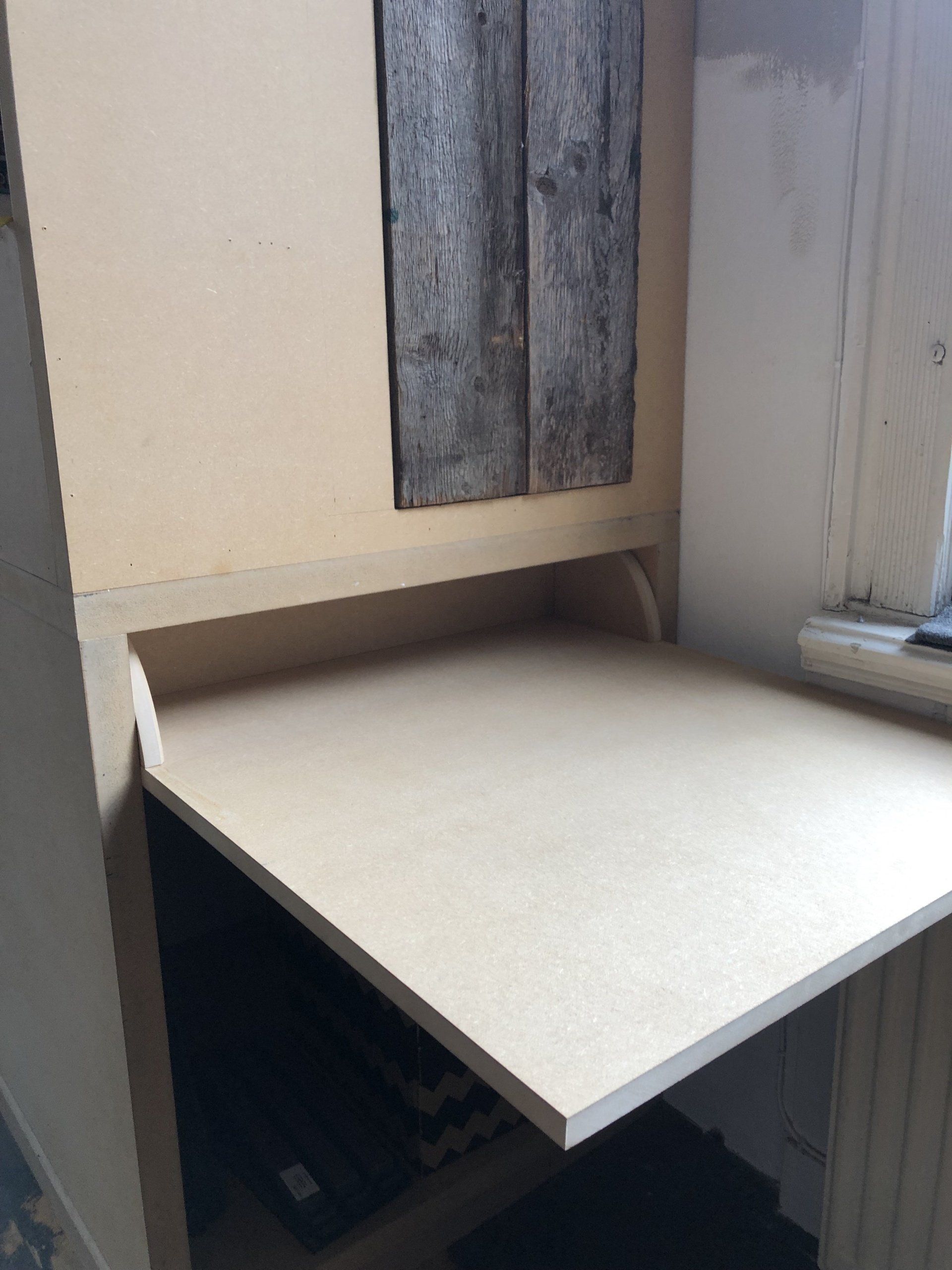 Een ingebouwd bureau met een lichtgekleurd blad in een hoek naast een raam.