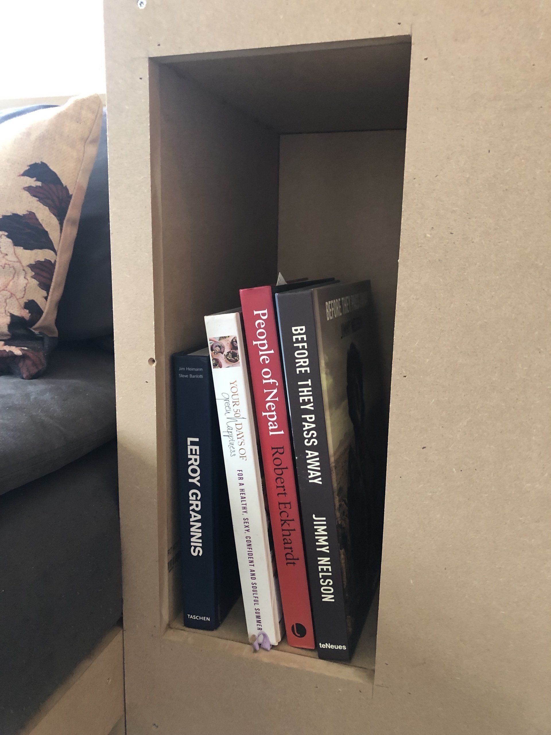Boekenplank met vier boeken. Bruine plank, donkerblauwe, witte, rode en zwarte ruggen van de boeken zichtbaar.
