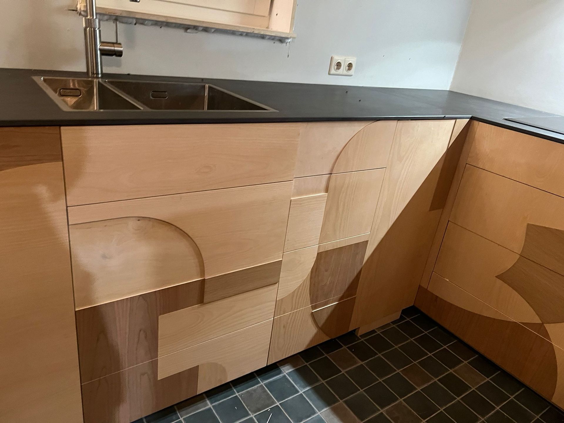 Keukenkastjes met een decoratief houten design, een grijs aanrechtblad en een roestvrijstalen spoelbak.