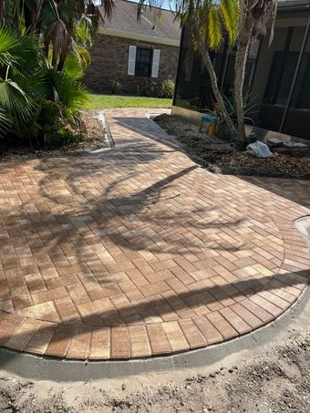 Paver walkway curves past a rock garden and connects to a driveway.