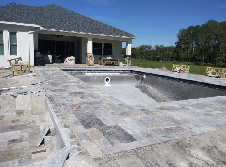 Pool construction site with gray stone coping, empty pool, and house in the background.