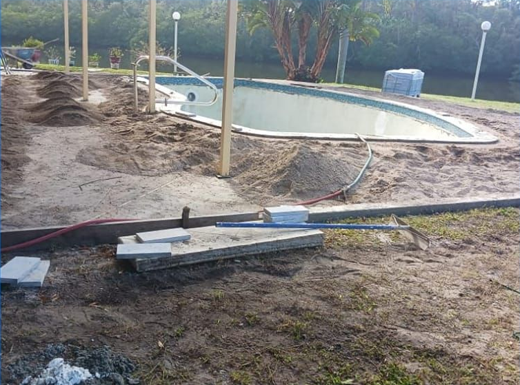 Pool under construction with sand, pavers, and pipes on the ground.