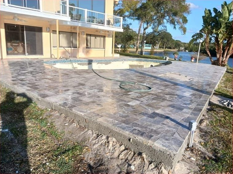 Patio with stone pavers and an empty pool next to a body of water.