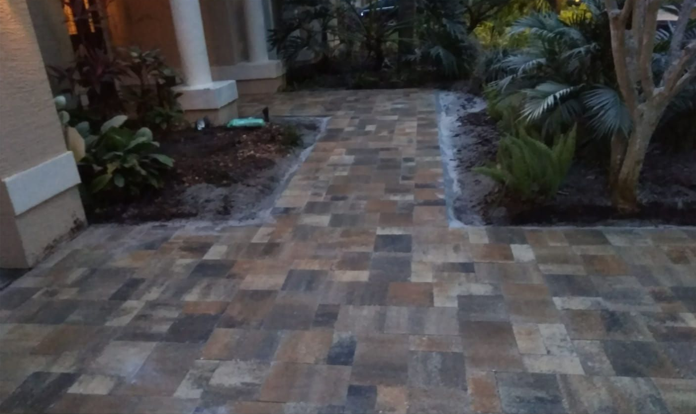 Brick pathway leading to a house entrance, bordered by landscaping.