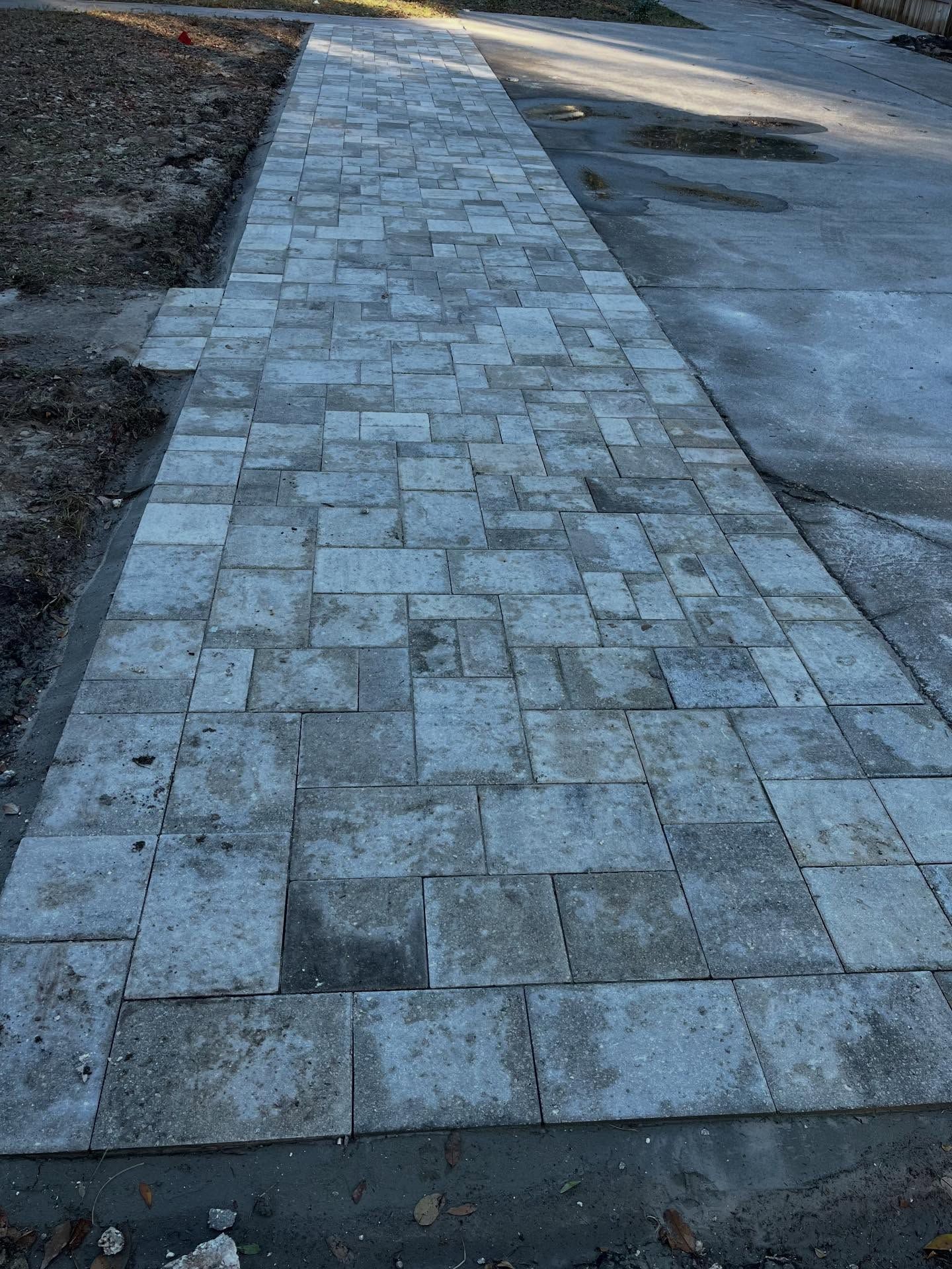 A pathway constructed of gray paving stones extending towards a paved road.