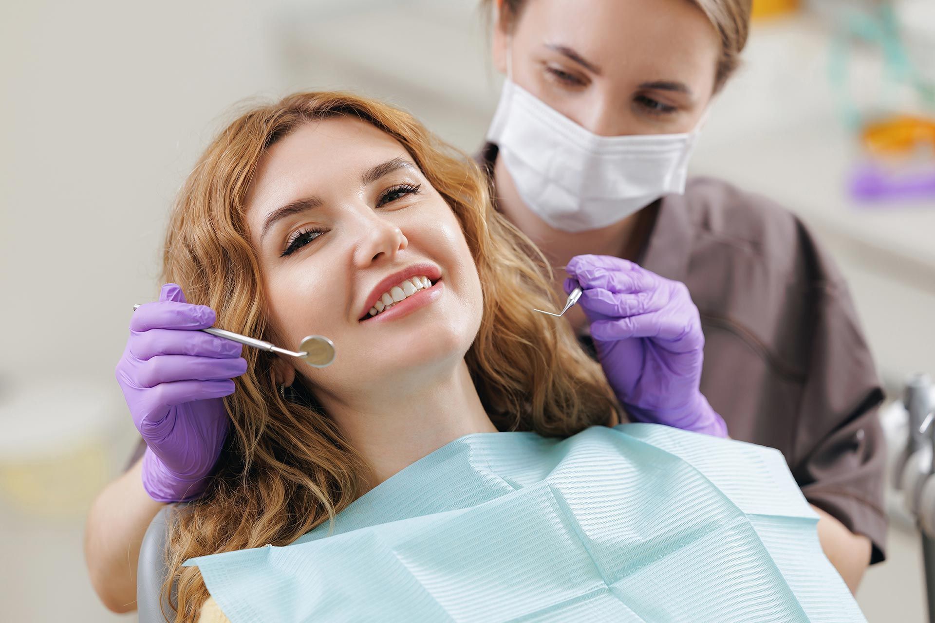 Dentist examining a smiling patient in a dental chair with gloved hands and a mouth mirror Dentist examining a smiling patient in a dental chair with gloved hands and a mouth mirror