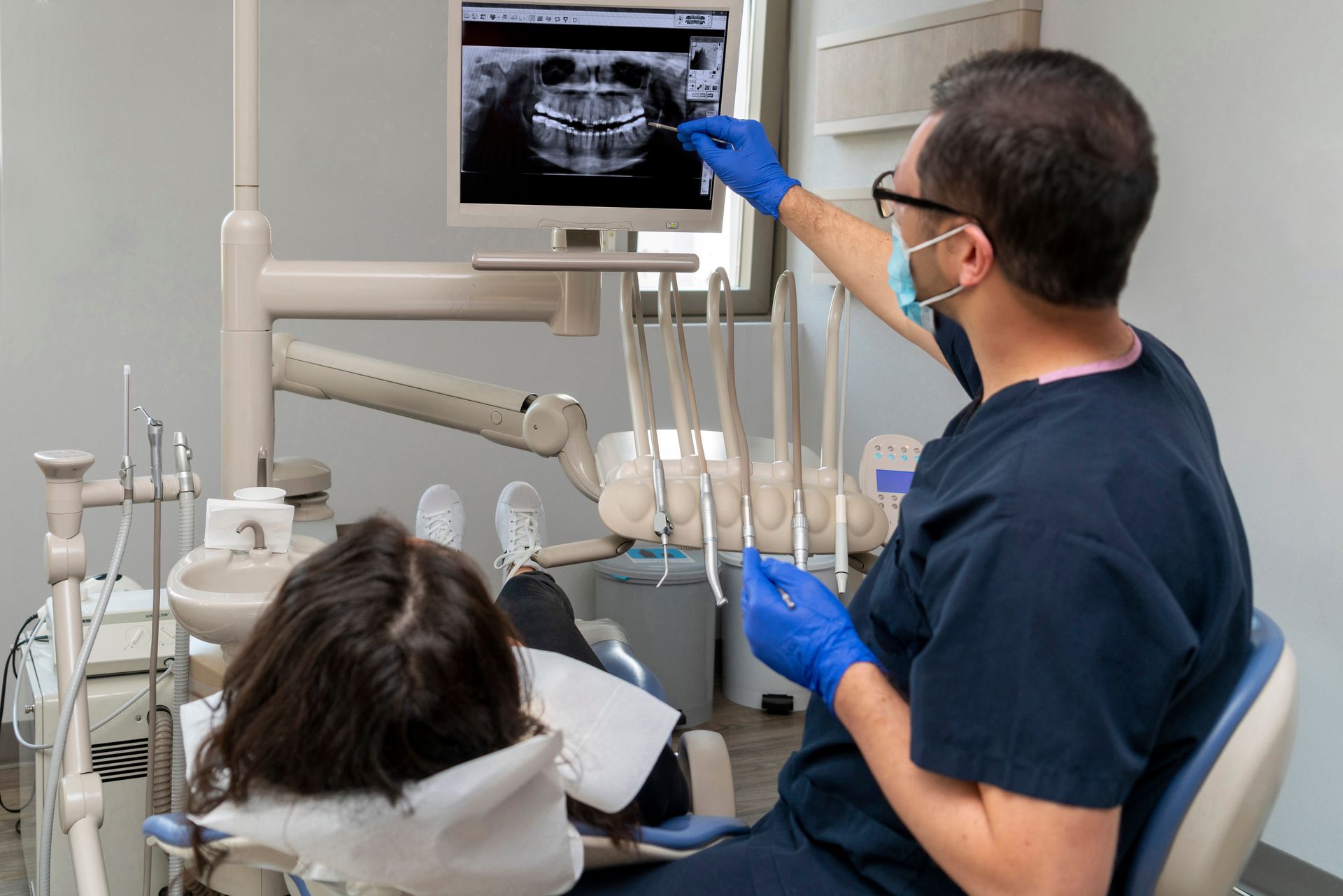 Dentist in scrubs and gloves reviewing a patient's dental X-ray on a monitor