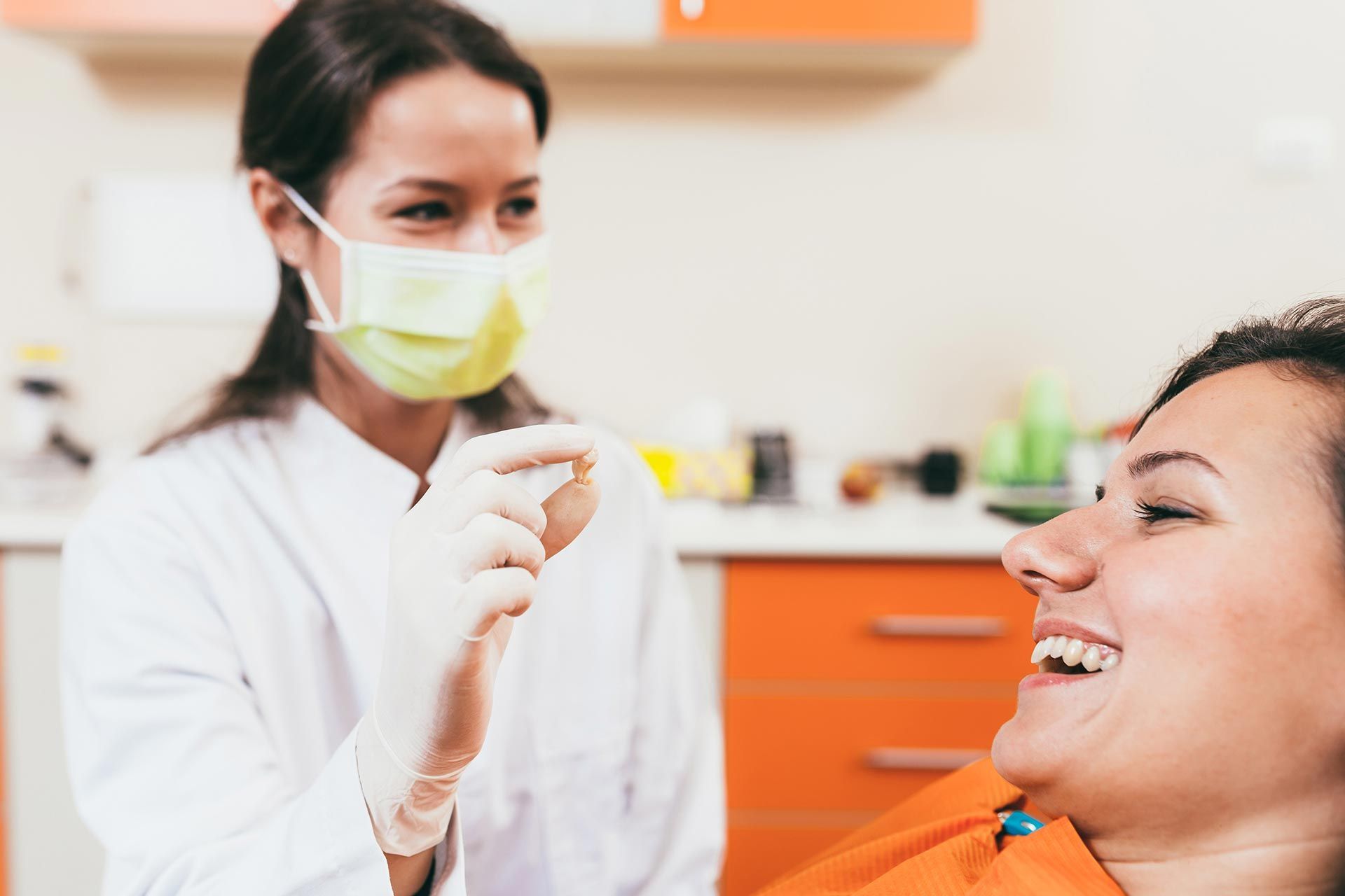 Dentist wearing a mask examines a smiling patient in an orange dental chair