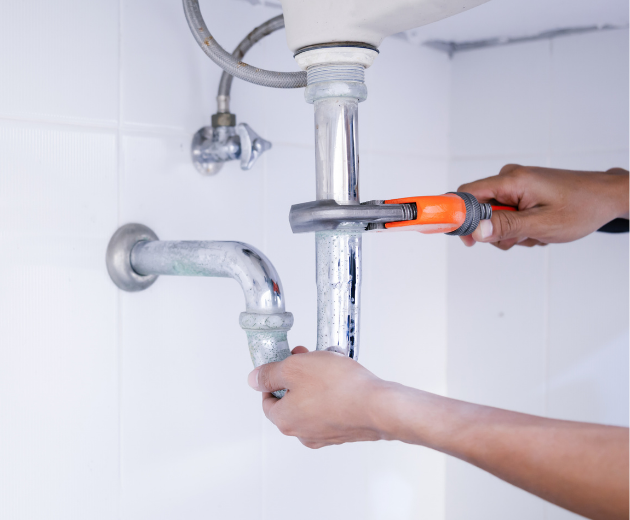 Hands using a pipe wrench to repair a silver bathroom sink drain pipe