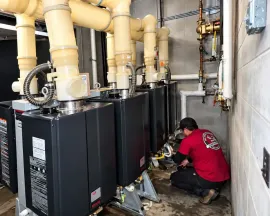 Technician in red shirt servicing HVAC units with large ductwork in an industrial room